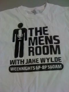 White T-shirt with black “The Men’s Room with Jake Wylde” radio show logo and schedule text.