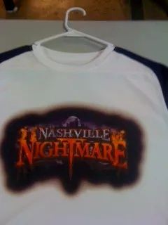 White T-shirt on a hanger with a “Nashville Nightmare” logo in orange and black.