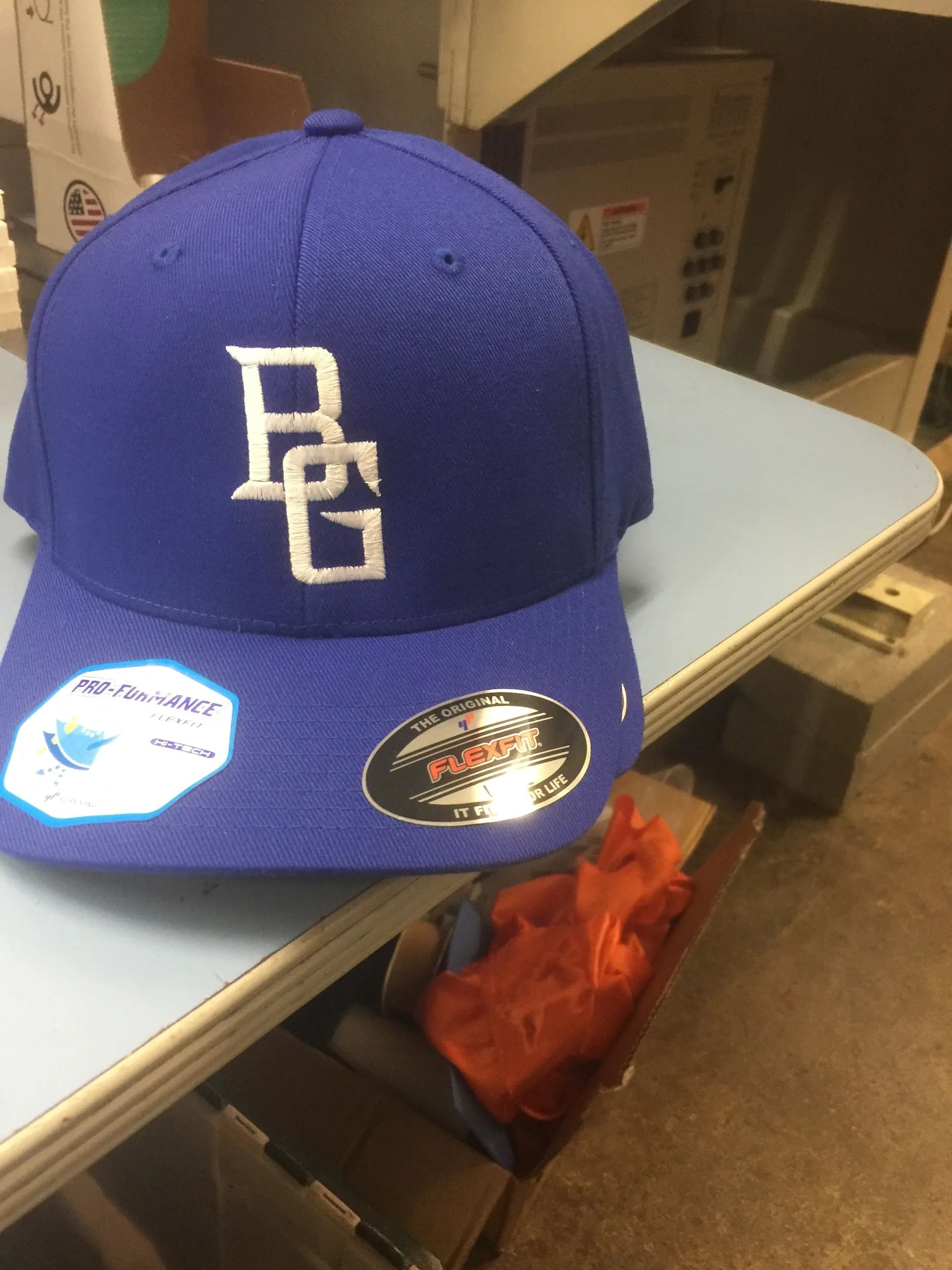 Blue baseball cap with a white logo, sitting on a table with two stickers on the brim.