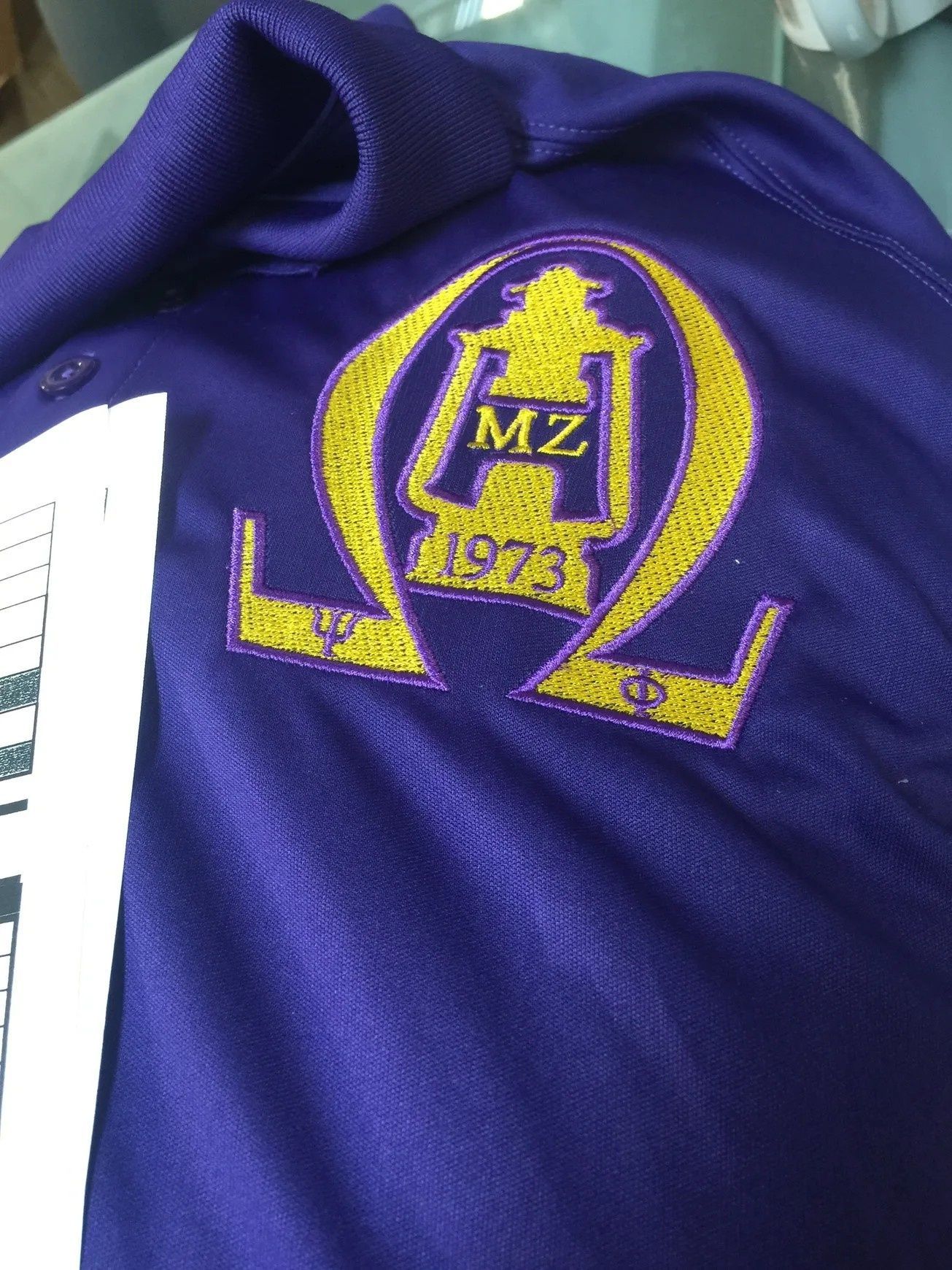 Purple fabric with a yellow embroidered Omega Psi Phi-style crest and “1973” on a garment