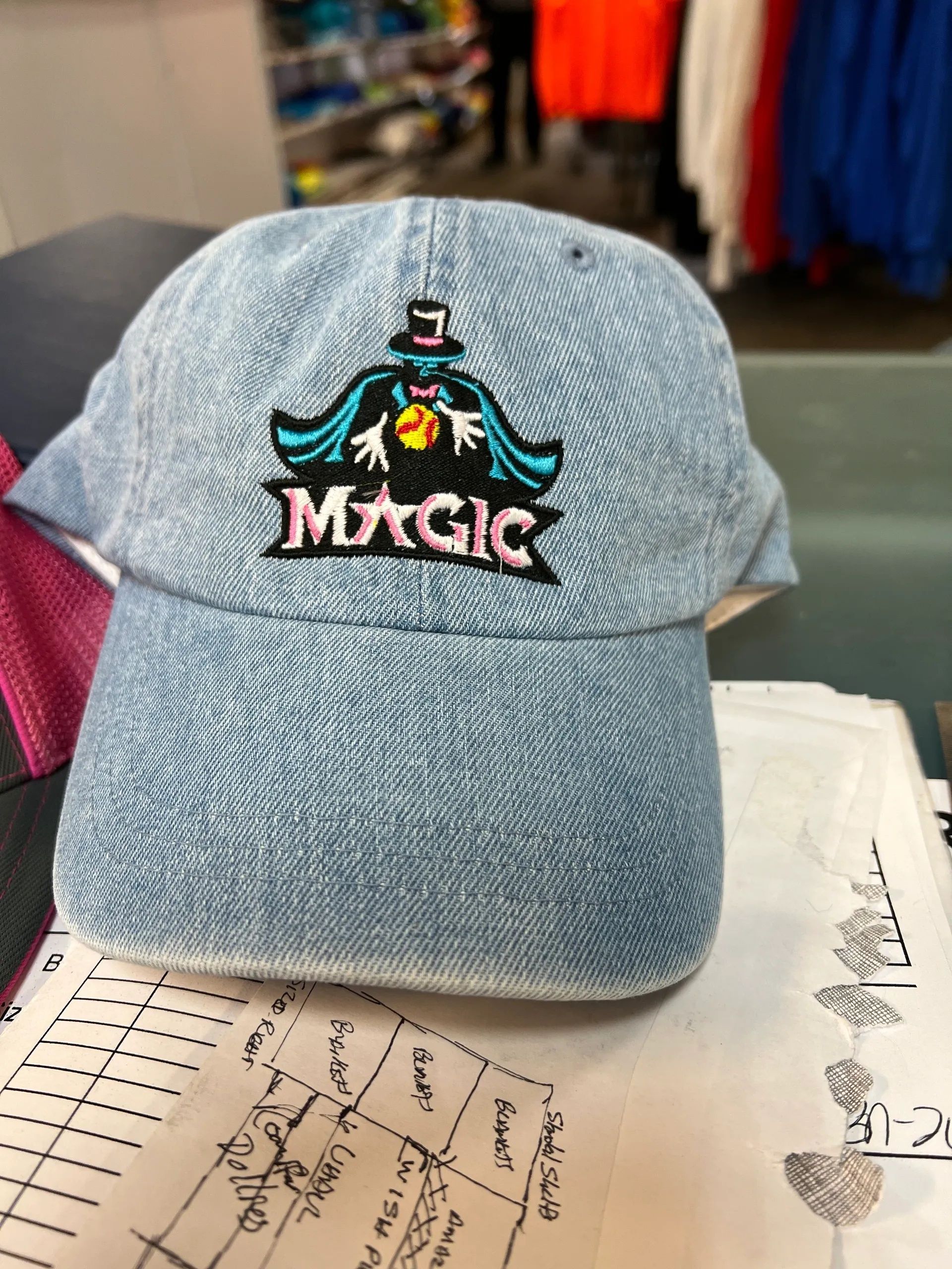 Blue denim cap with a colorful Magic logo, resting on a notebook indoors.