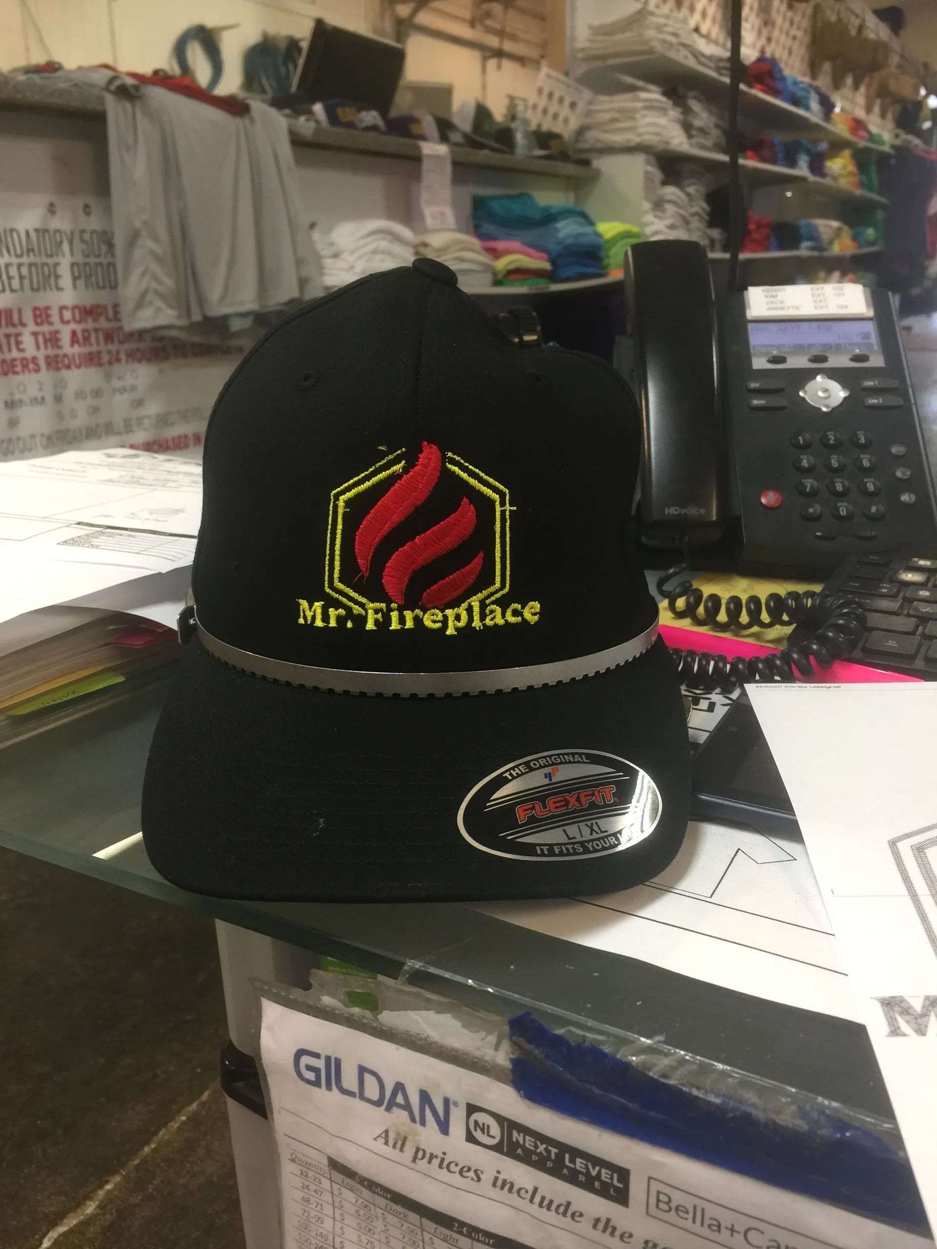 Black Mr. Firefighter cap on a cluttered desk beside a phone and clothing boxes
