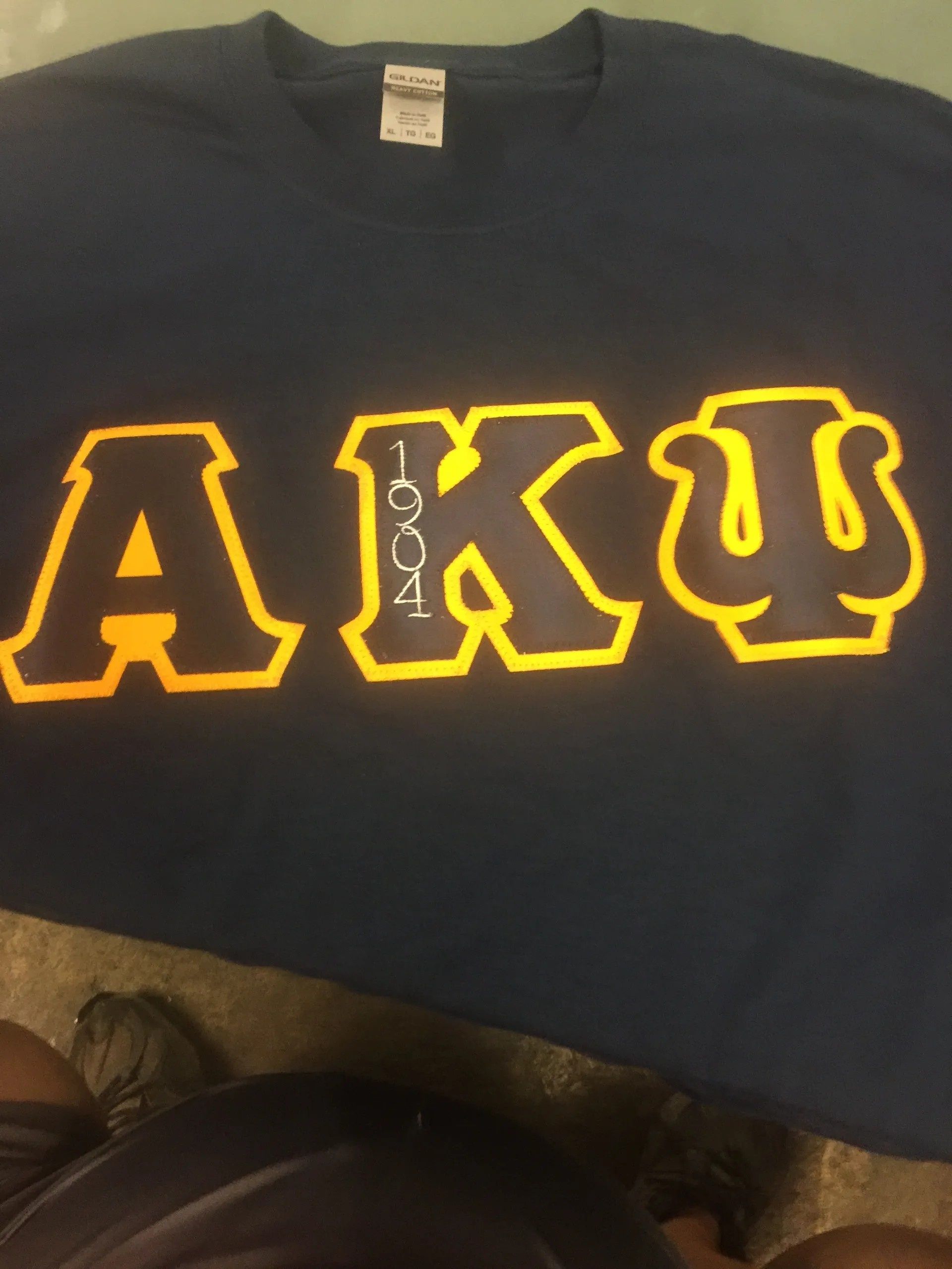 Black sweatshirt with large gold outlined Greek letters across the chest.