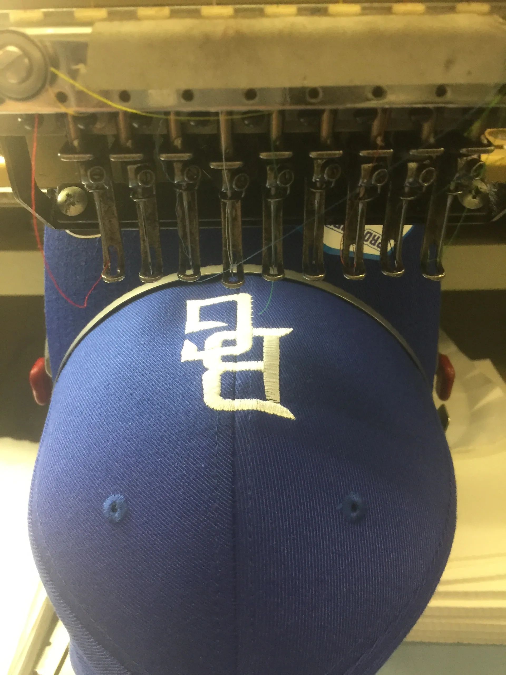 Embroidery machine stitching a white logo onto a blue baseball cap