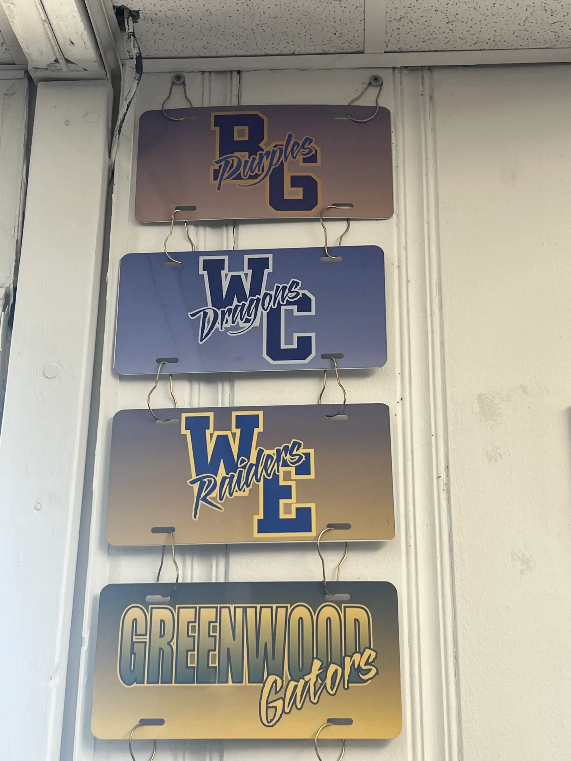 Four stacked school signs reading B, W, C, and Greenwood above a hallway wall