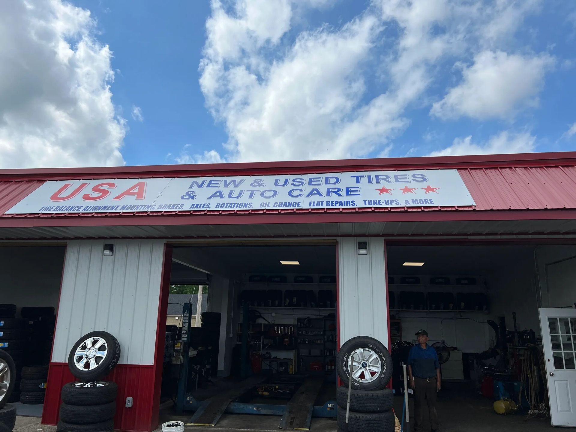 Auto repair shop storefront with open bays, cars, and a USA Used Tire and Auto Care sign under a blue sky