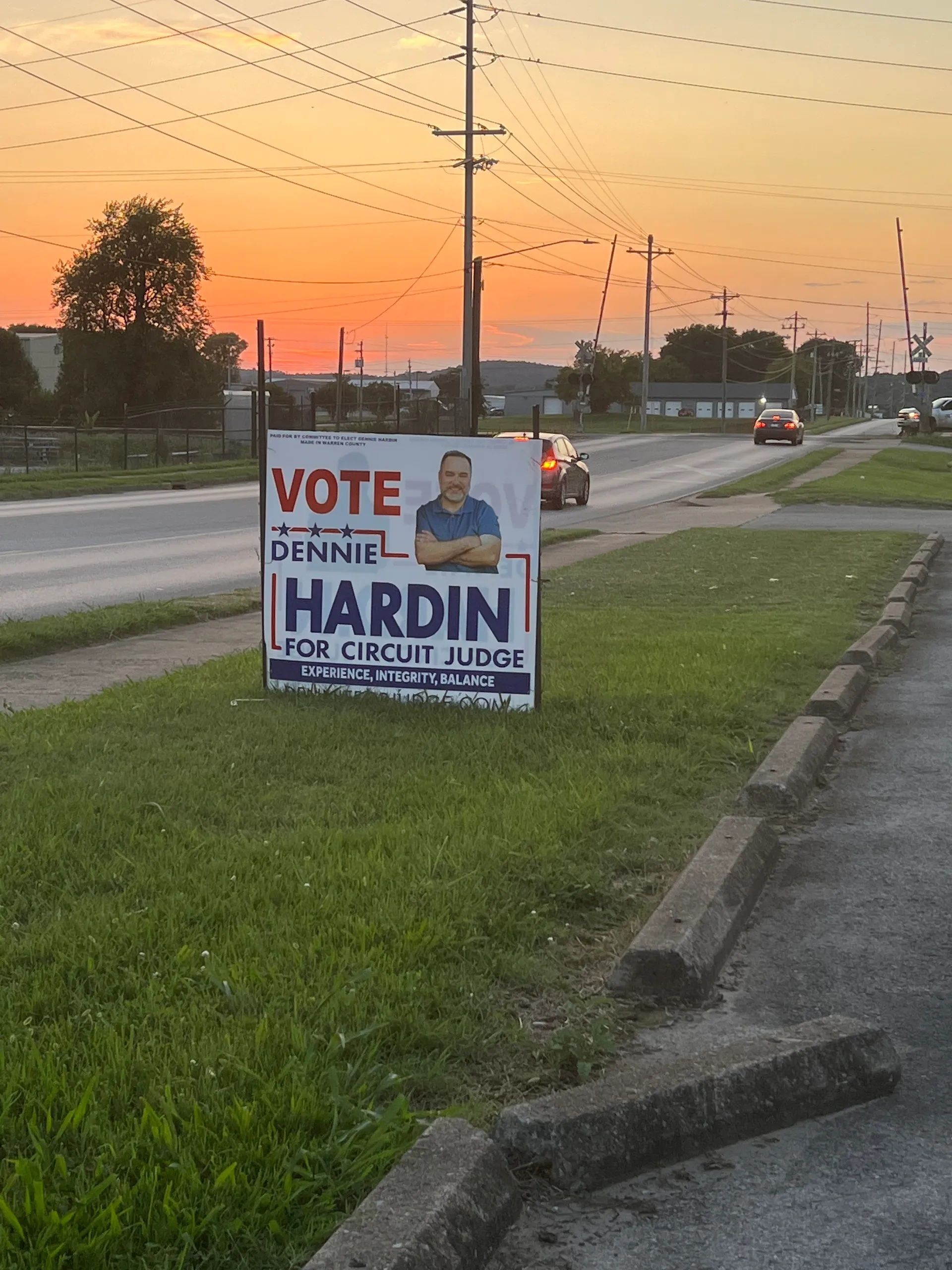 Political yard sign for Denise Hardin at a roadside in front of a grassy field at sunset