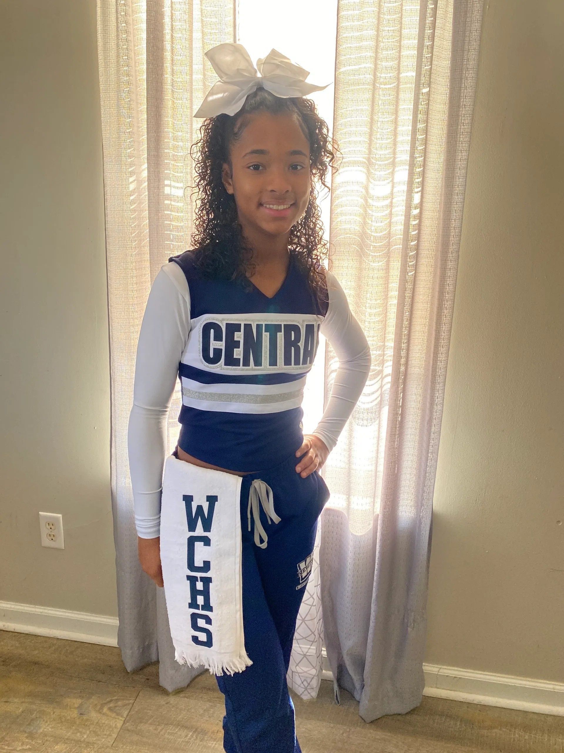 Cheerleader in blue and white uniform standing indoors in front of curtains.