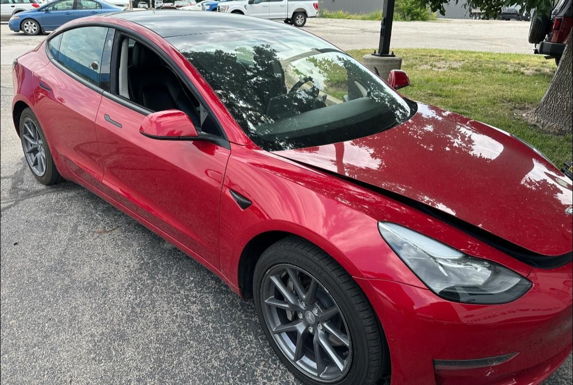 Red Tesla car with front-end damage parked on the street.