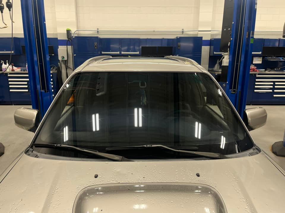 Silver car in a garage, seen from the front. Windshield wipers up. Lift arms in the background.