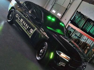 Black car with green lights, Glenn's Autoglass logo, parked inside a shop with glass.