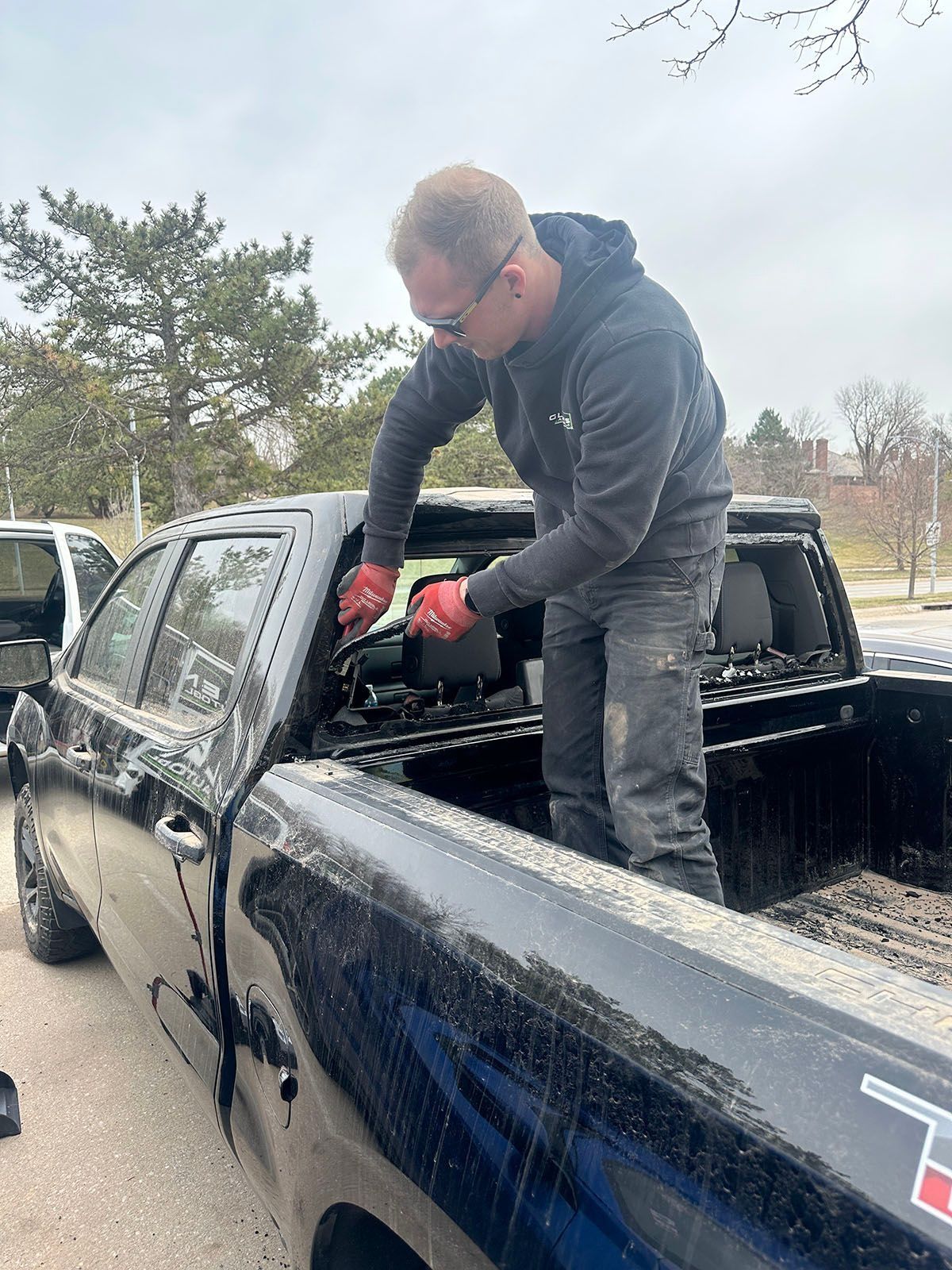 Man in red gloves working on a black truck bed in a driveway on an overcast day.