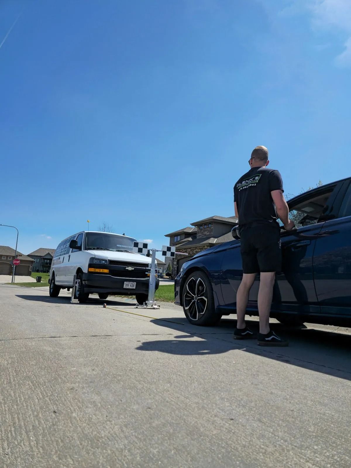 Man next to a blue car, near a white van with a finish line banner on a residential street on a sunny day.