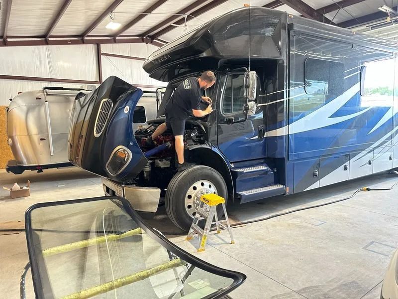 A mechanic working on a blue RV, replacing the windshield in a repair shop.