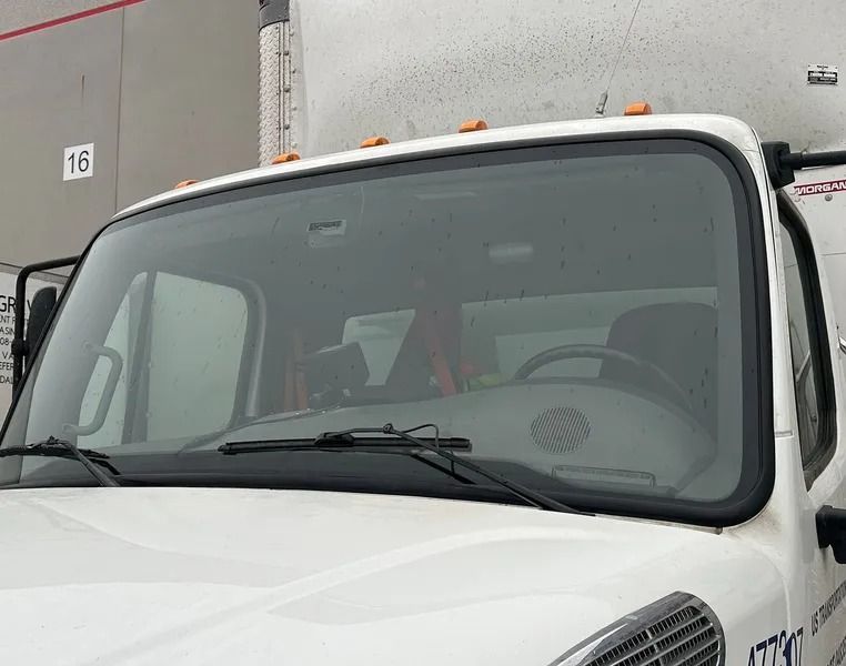 Close-up of the front of a white delivery truck with wipers and tinted windshield.
