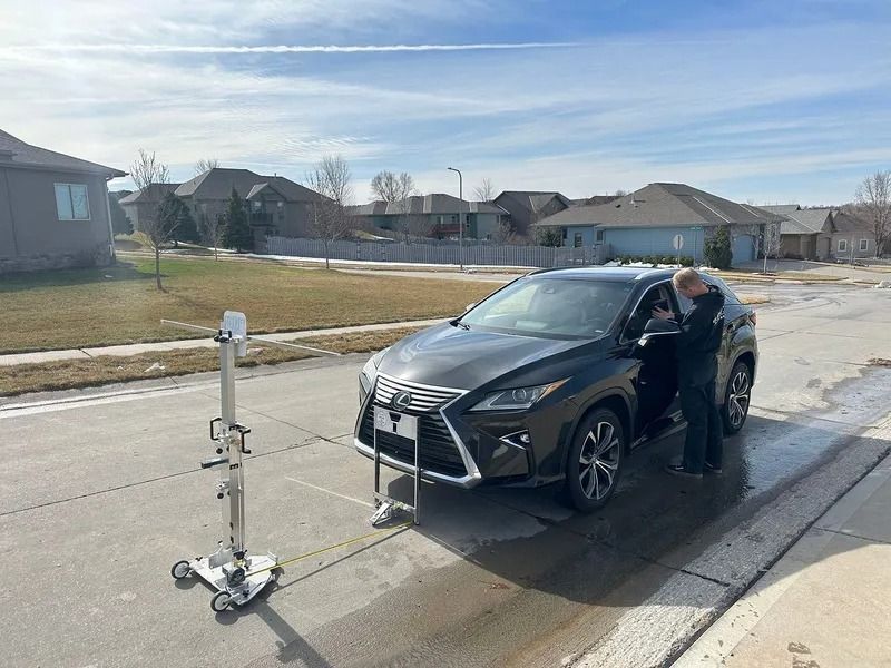 A person entering a dark SUV next to a metal device on a residential street, sunny day.