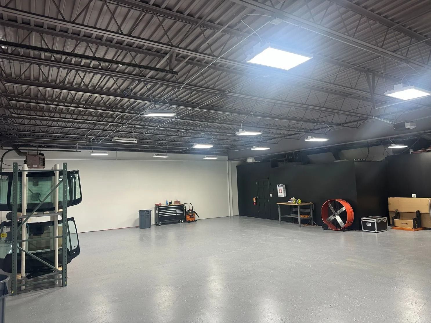 Large empty industrial space with a white wall, dark walls, and equipment.