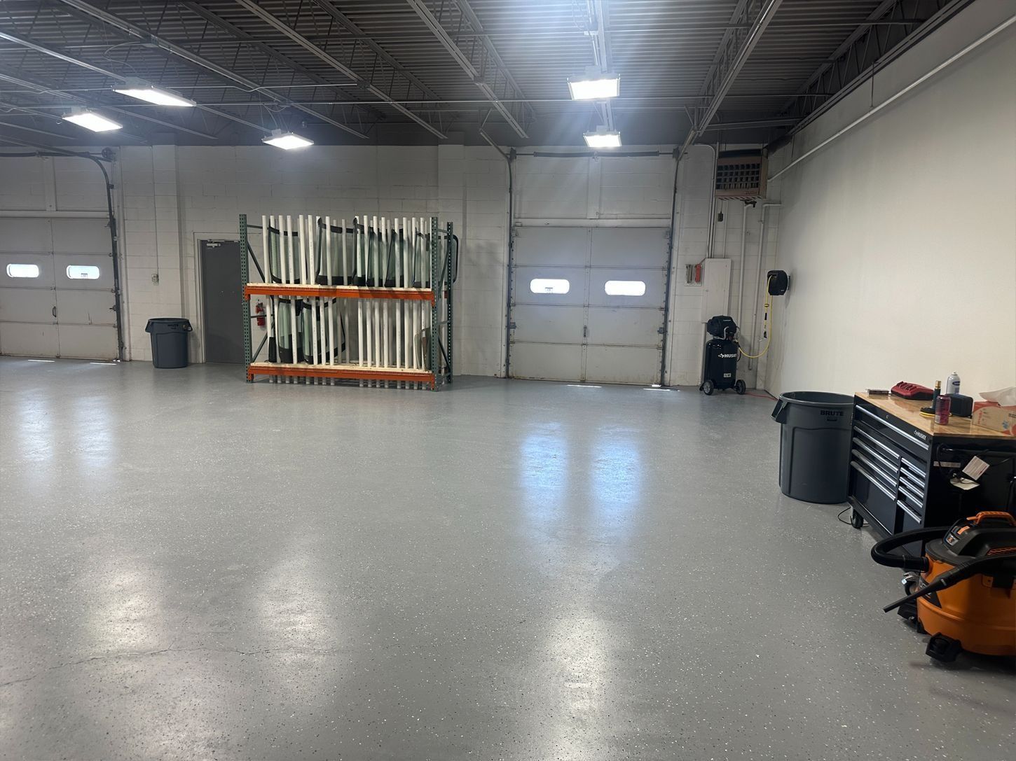 Interior view of a gray-floored warehouse with bay doors, shelving, and a workbench.