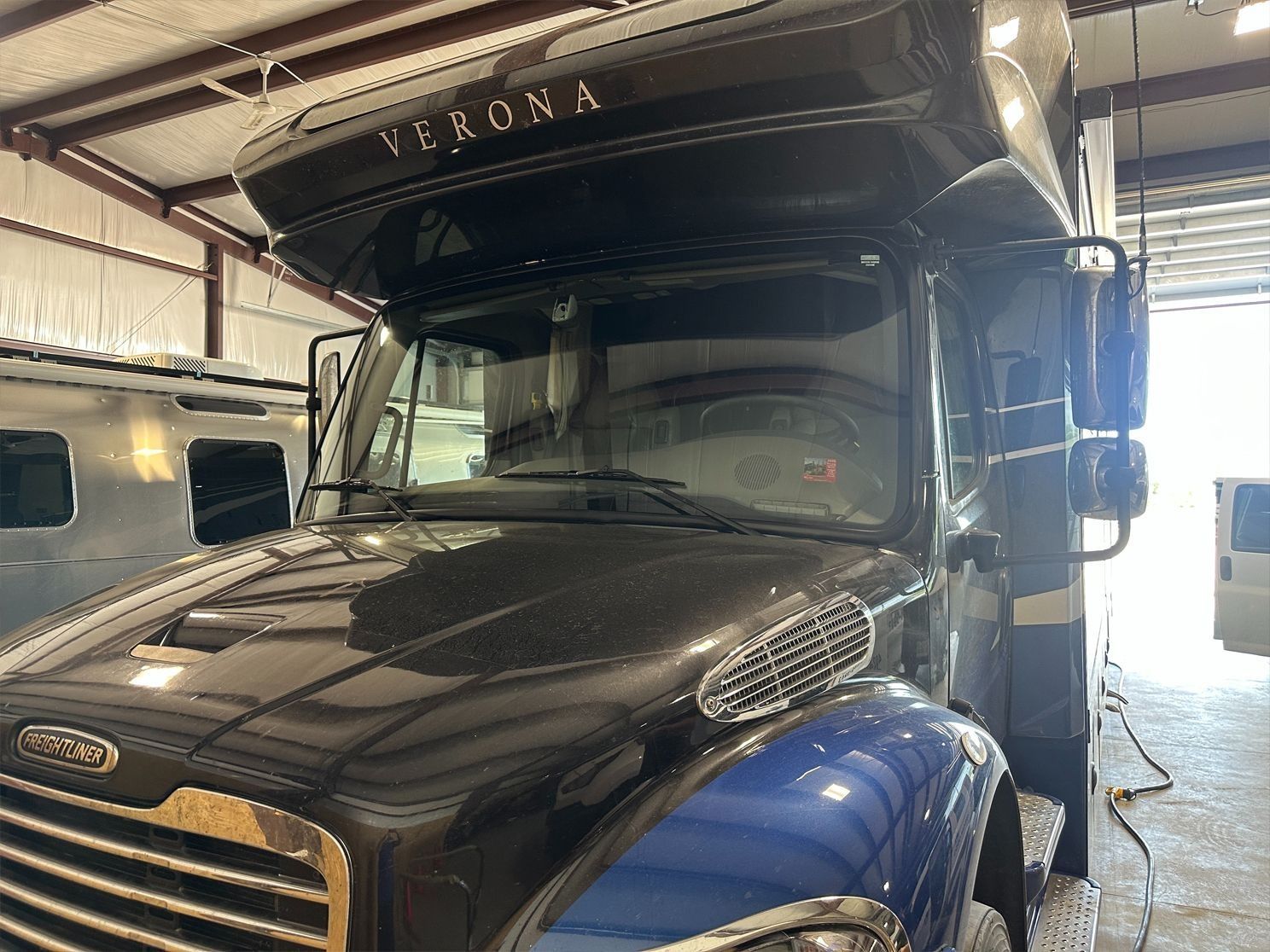 Dark Verona RV, parked in garage. Black and blue exterior, front view.