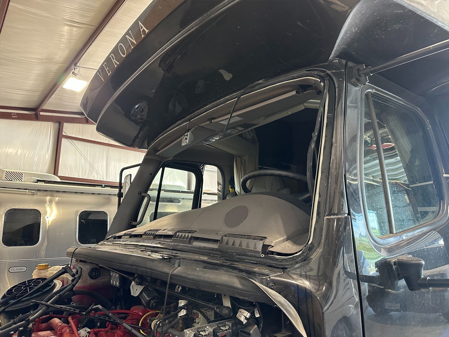 Damaged RV windshield with exposed engine, parked in a shop.