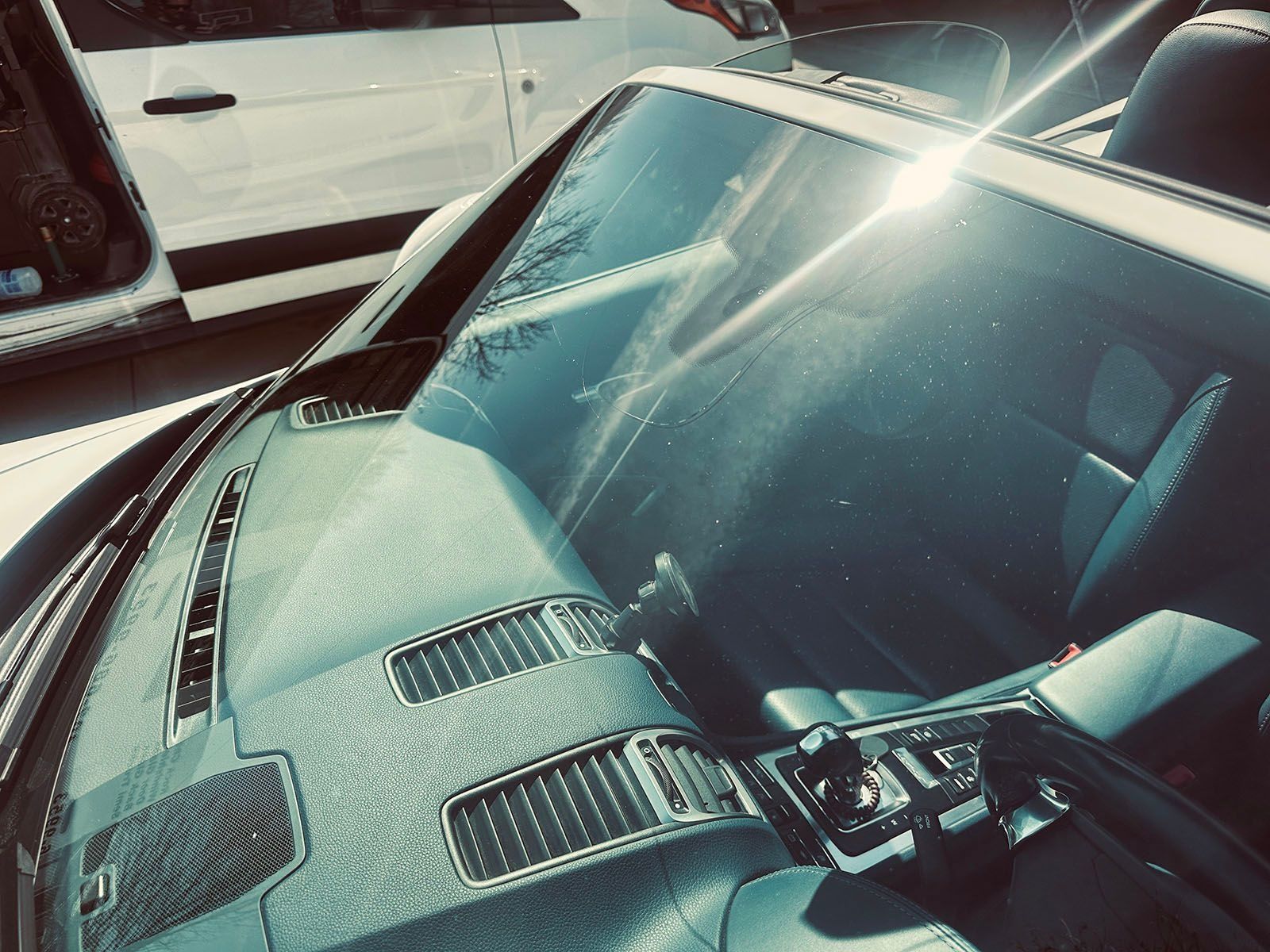 Interior of a white convertible car with a sunlit windshield and black dashboard.