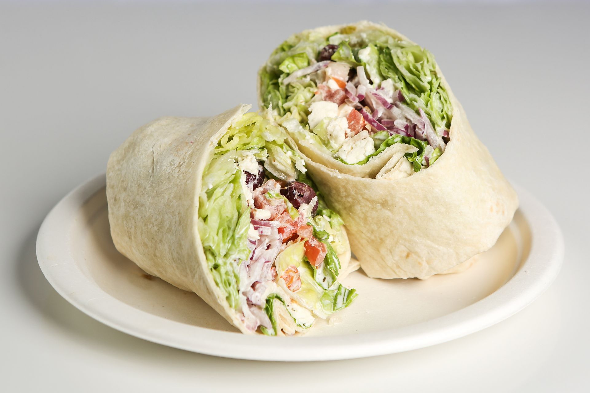 A wrap with lettuce, tomatoes, and other vegetables on a white plate.