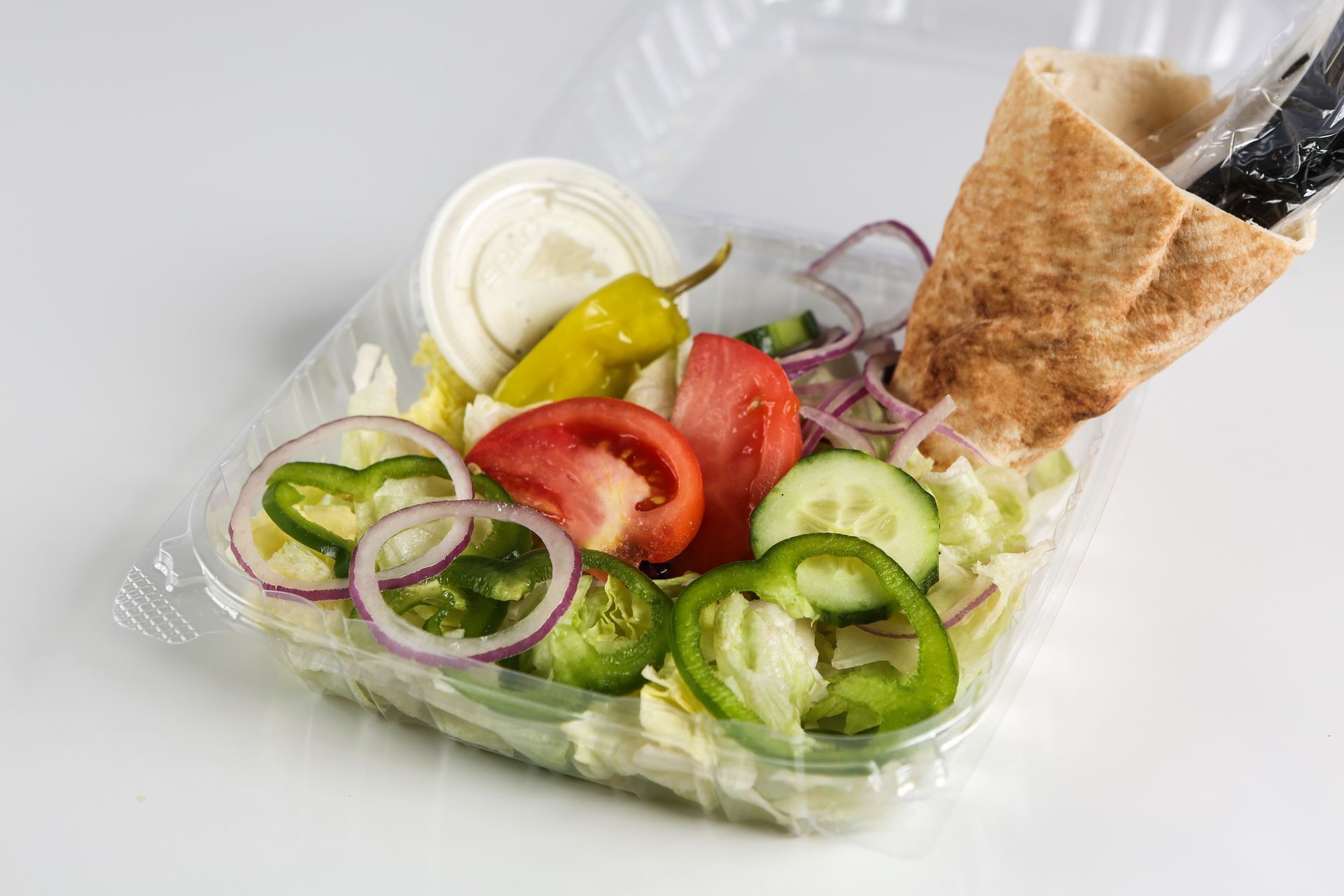 A plastic container filled with vegetables and pita bread.