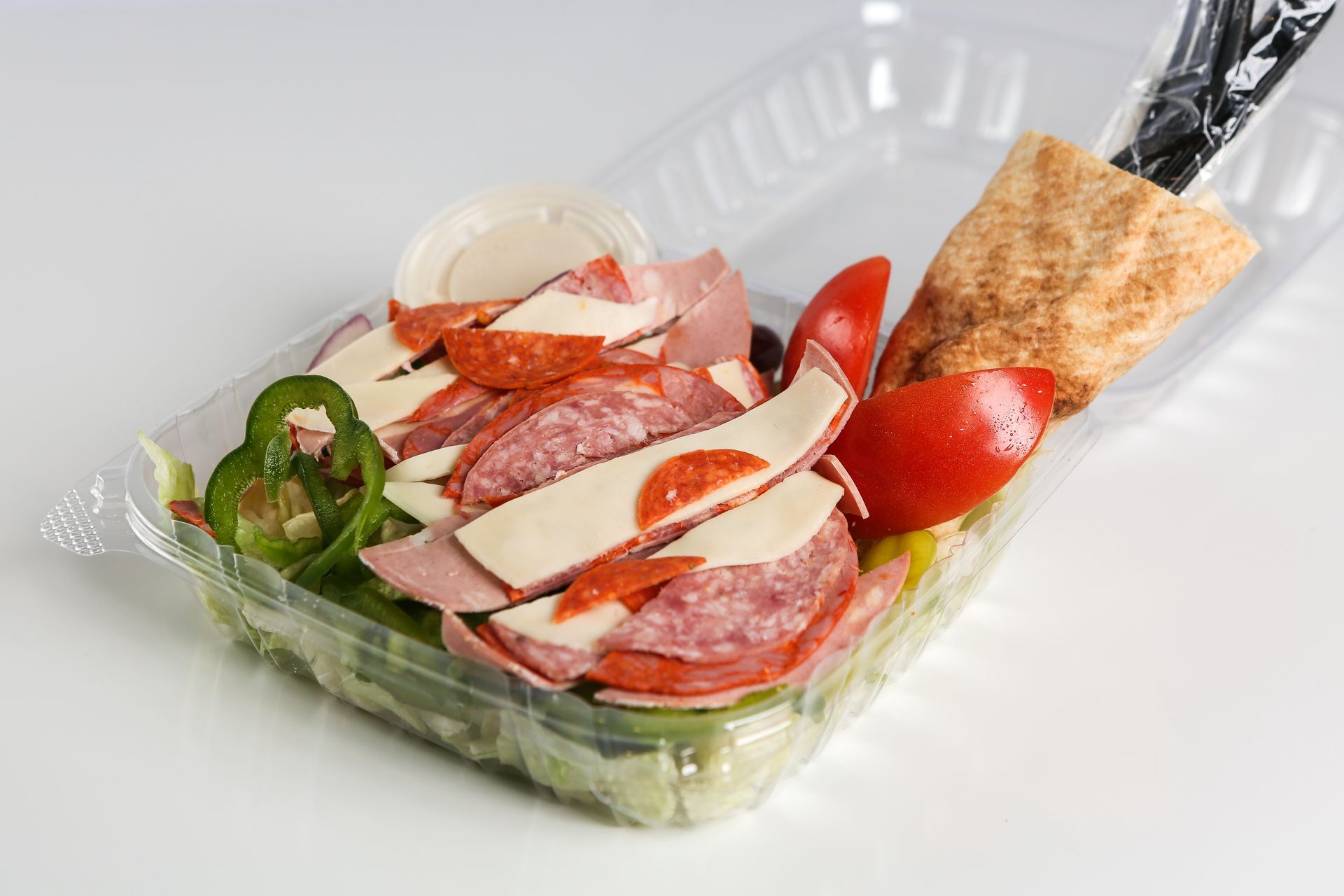 A plastic container filled with a salad with meat, cheese, tomatoes, and peppers.