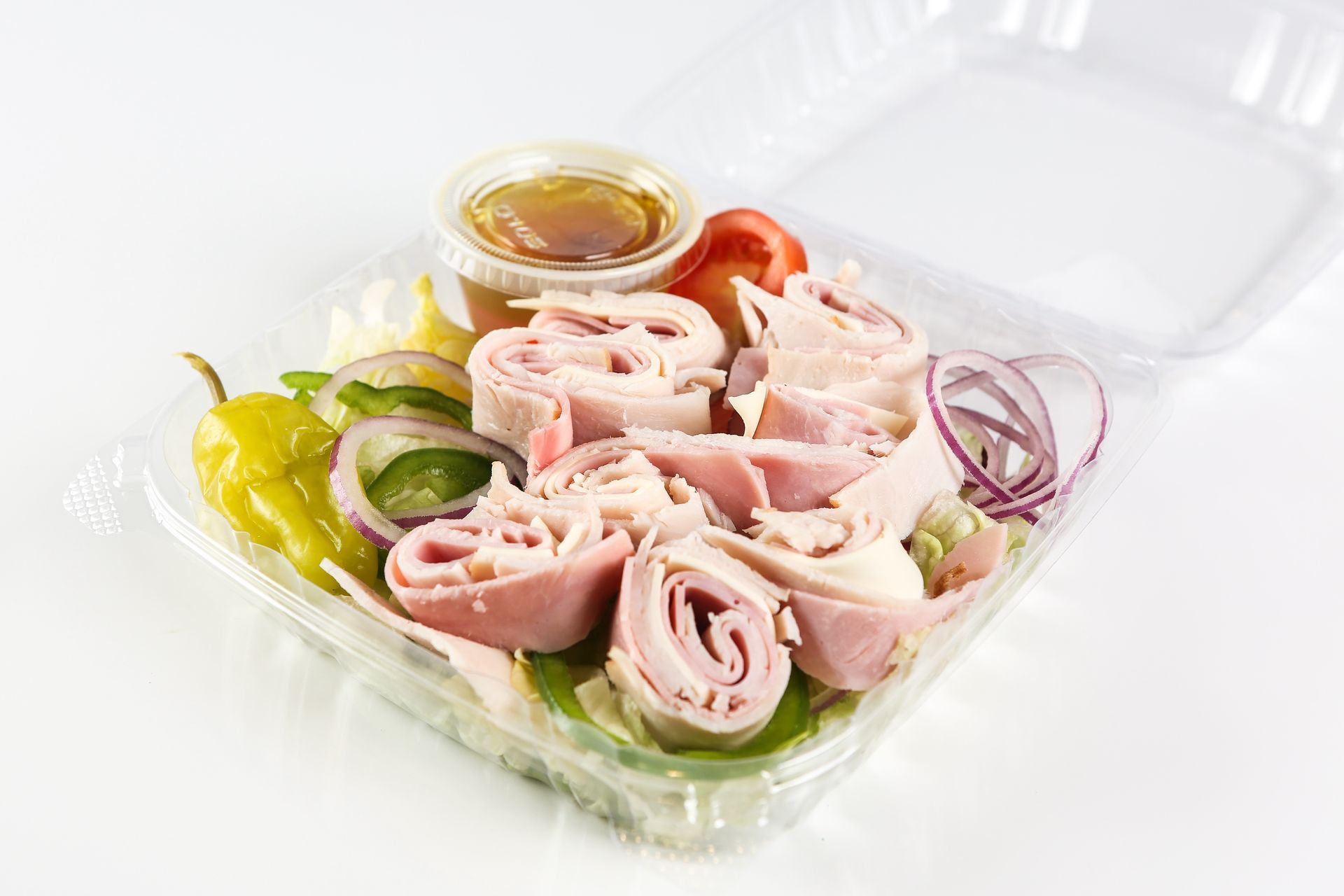 A plastic container filled with a salad with ham, peppers, onions, and tomatoes.