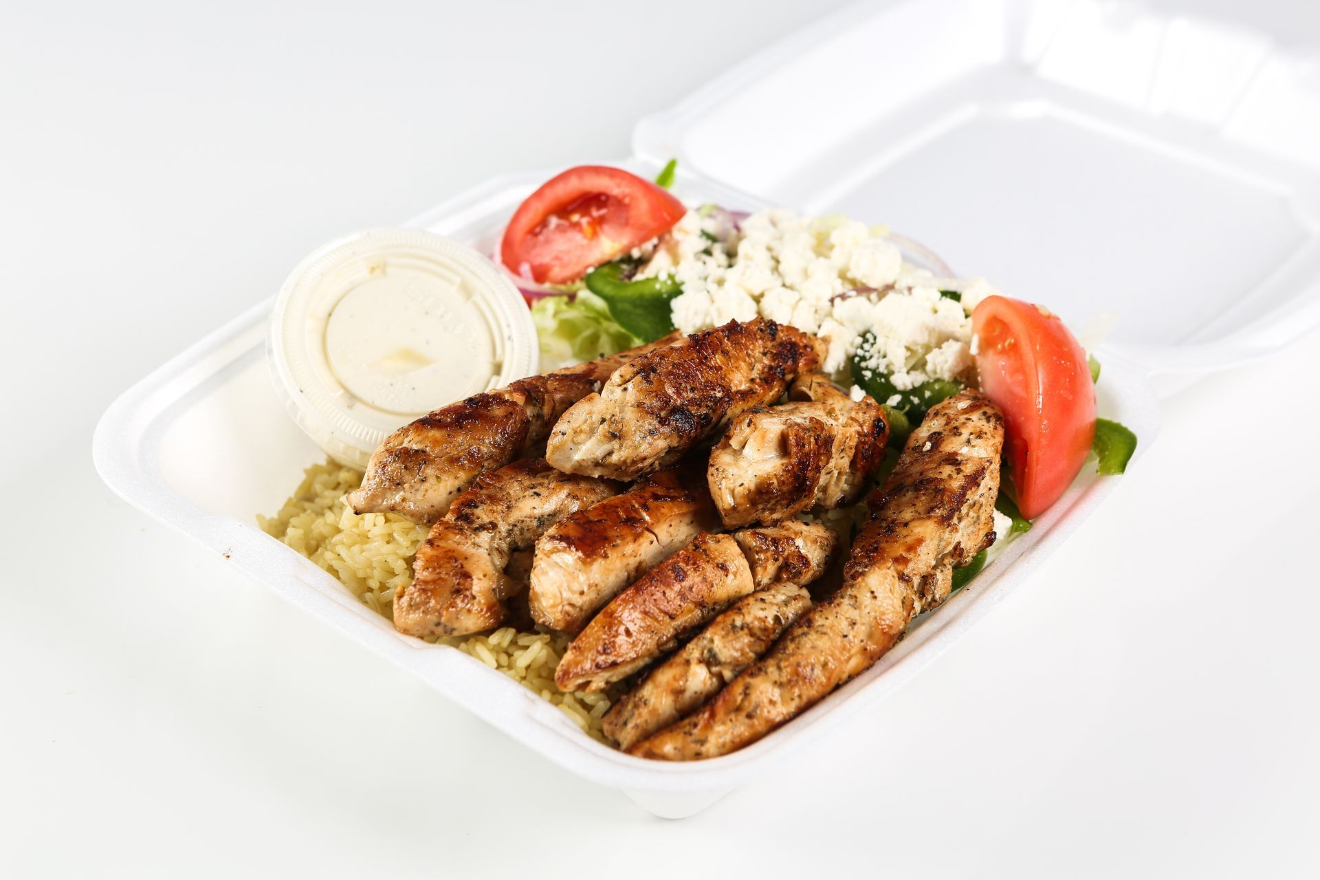 A styrofoam container filled with chicken, rice, tomatoes, and feta cheese.