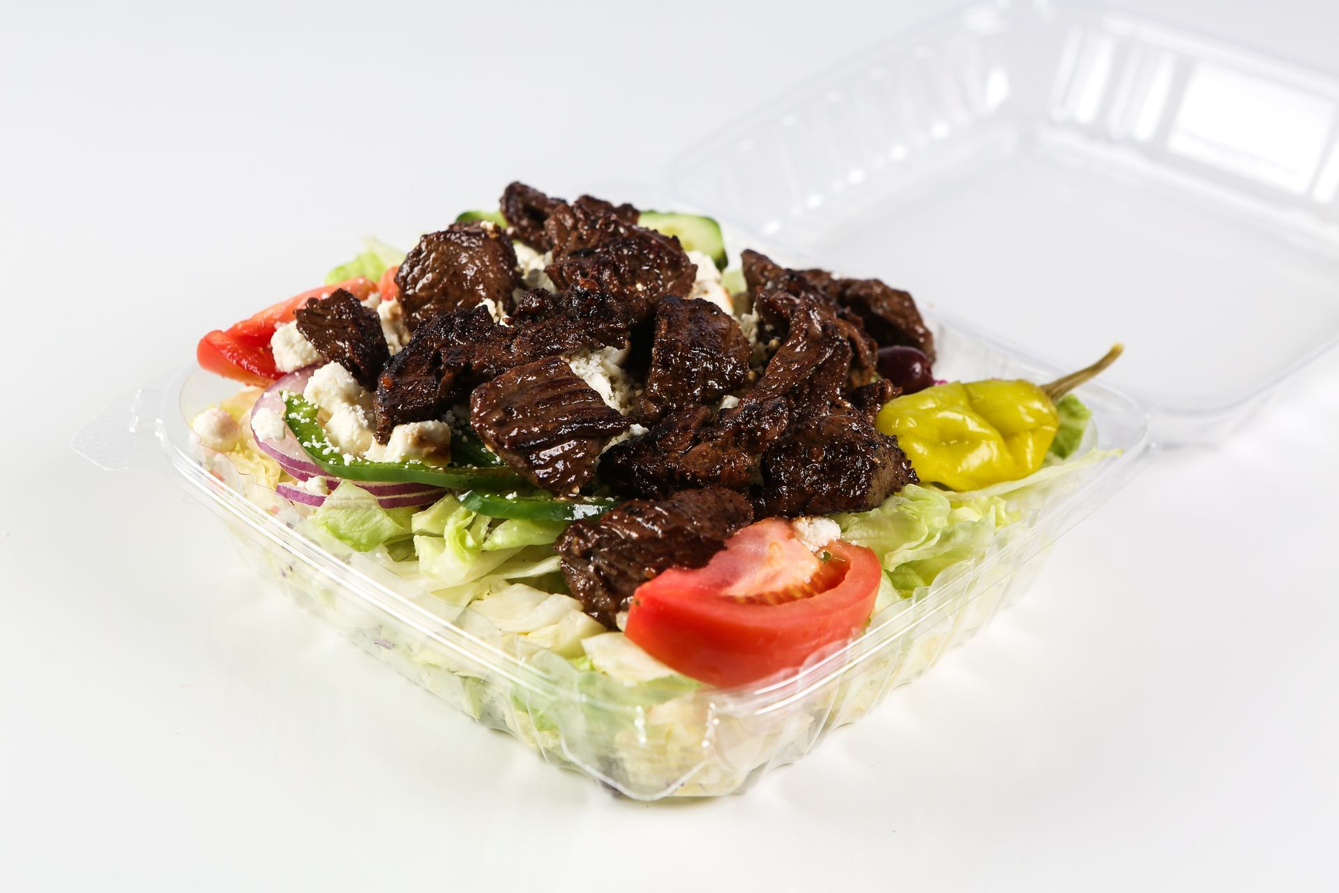 A close-up of a salad in a plastic container on a table.