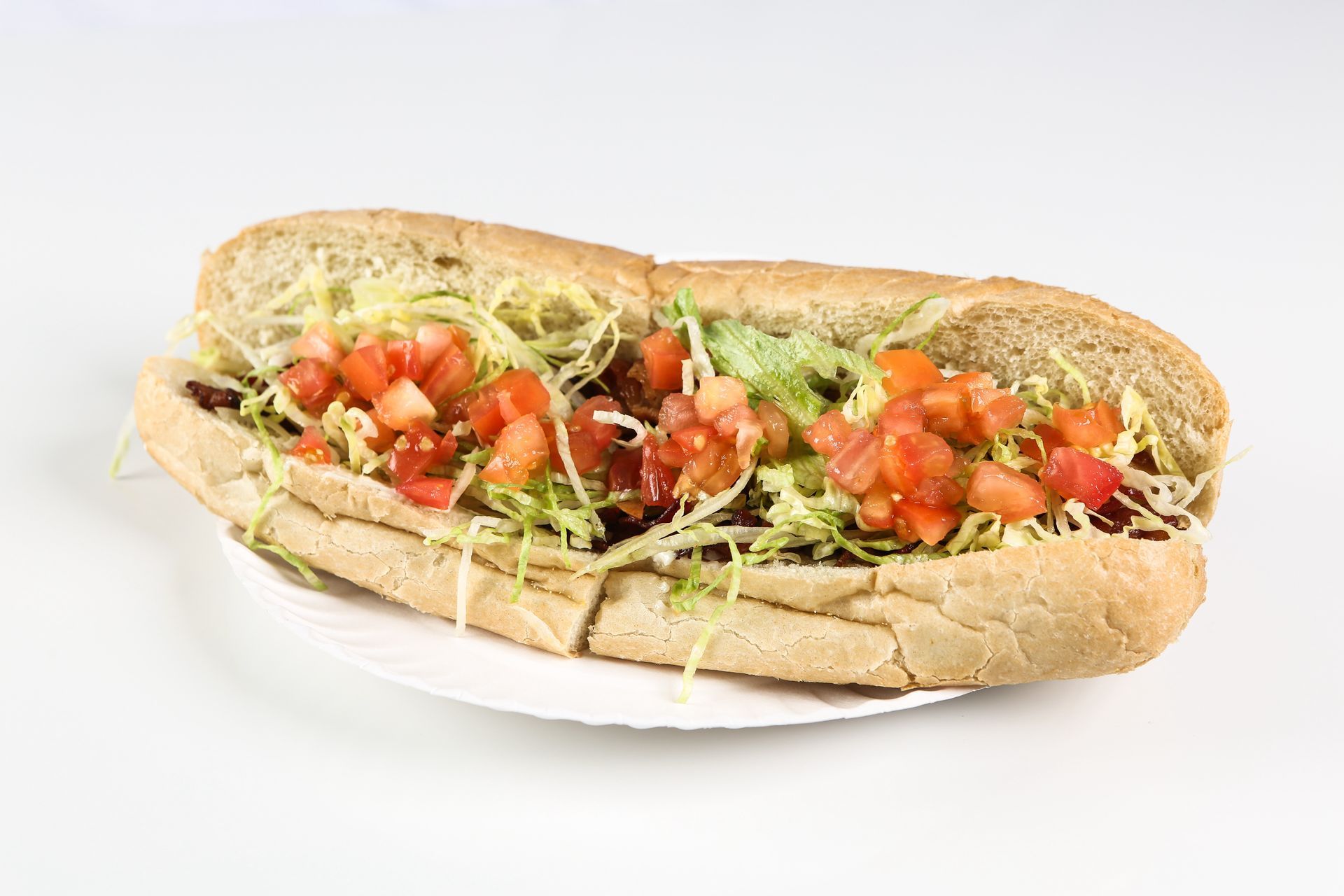 A sub sandwich with lettuce , tomatoes, and cheese on a paper plate.
