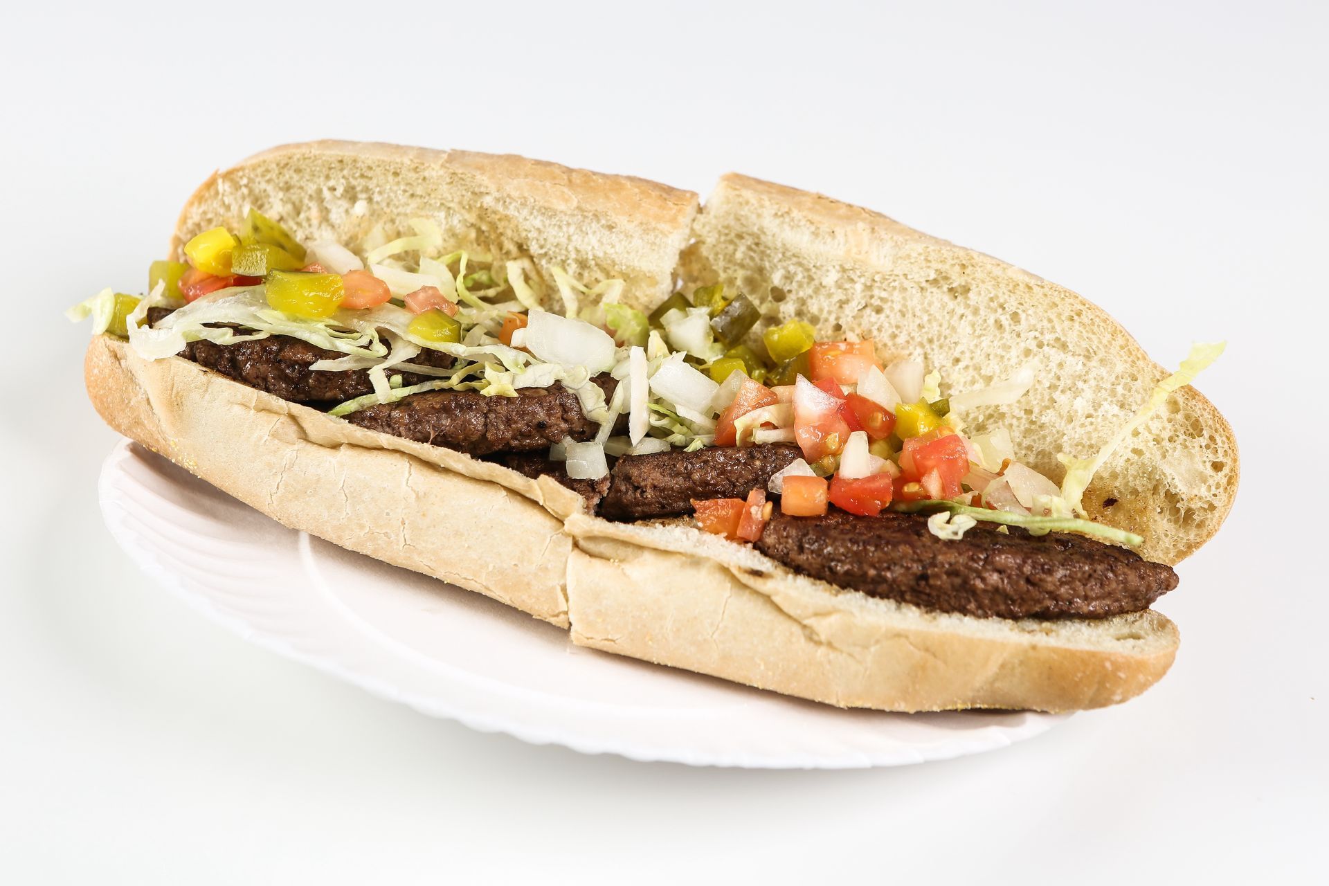 A sub sandwich with lettuce, tomatoes, and onions on a white plate.