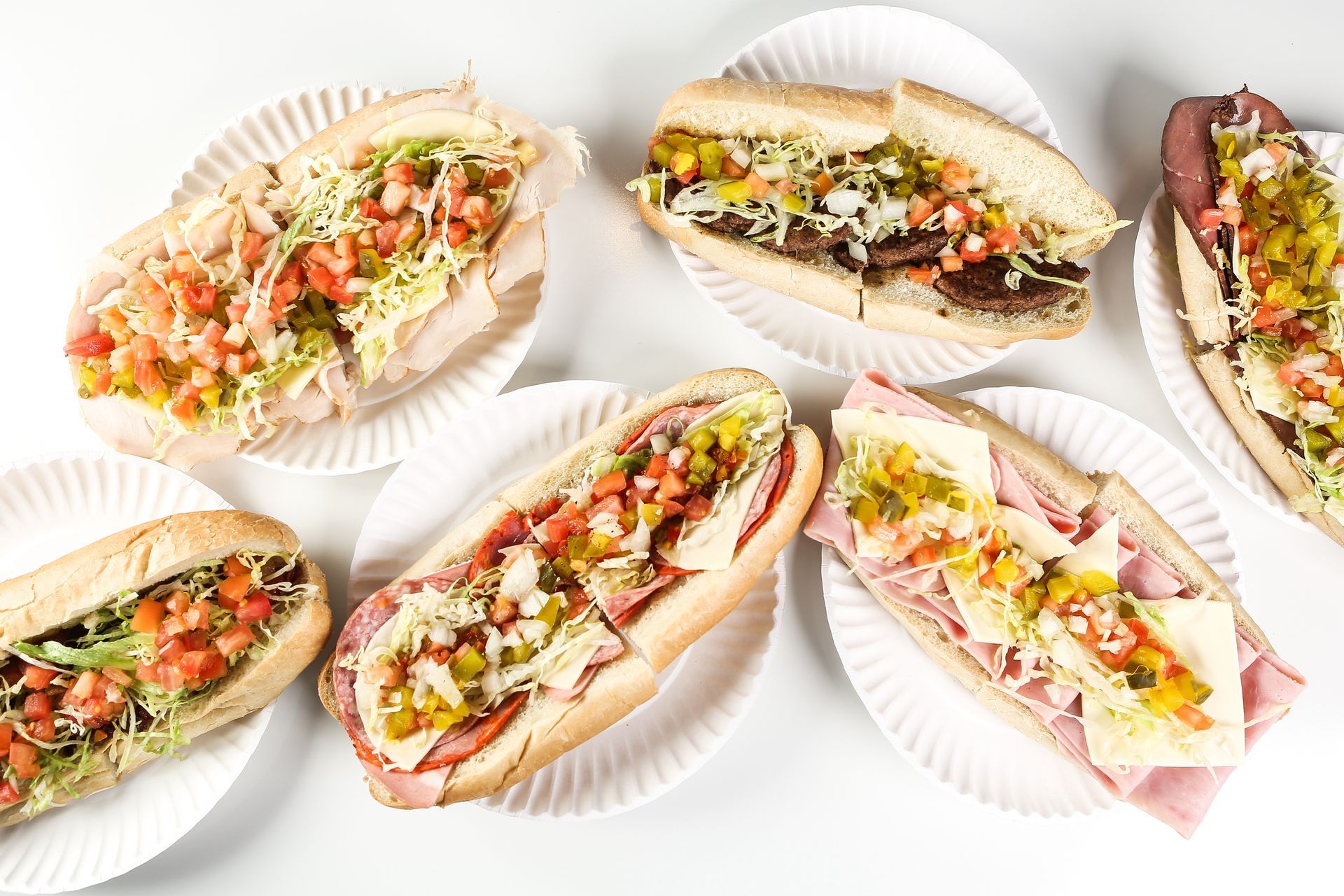 A variety of sub sandwiches are sitting on paper plates on a table.