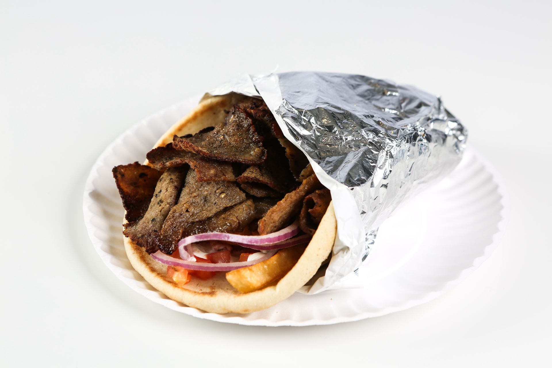 A gyro sandwich wrapped in tin foil on a paper plate.