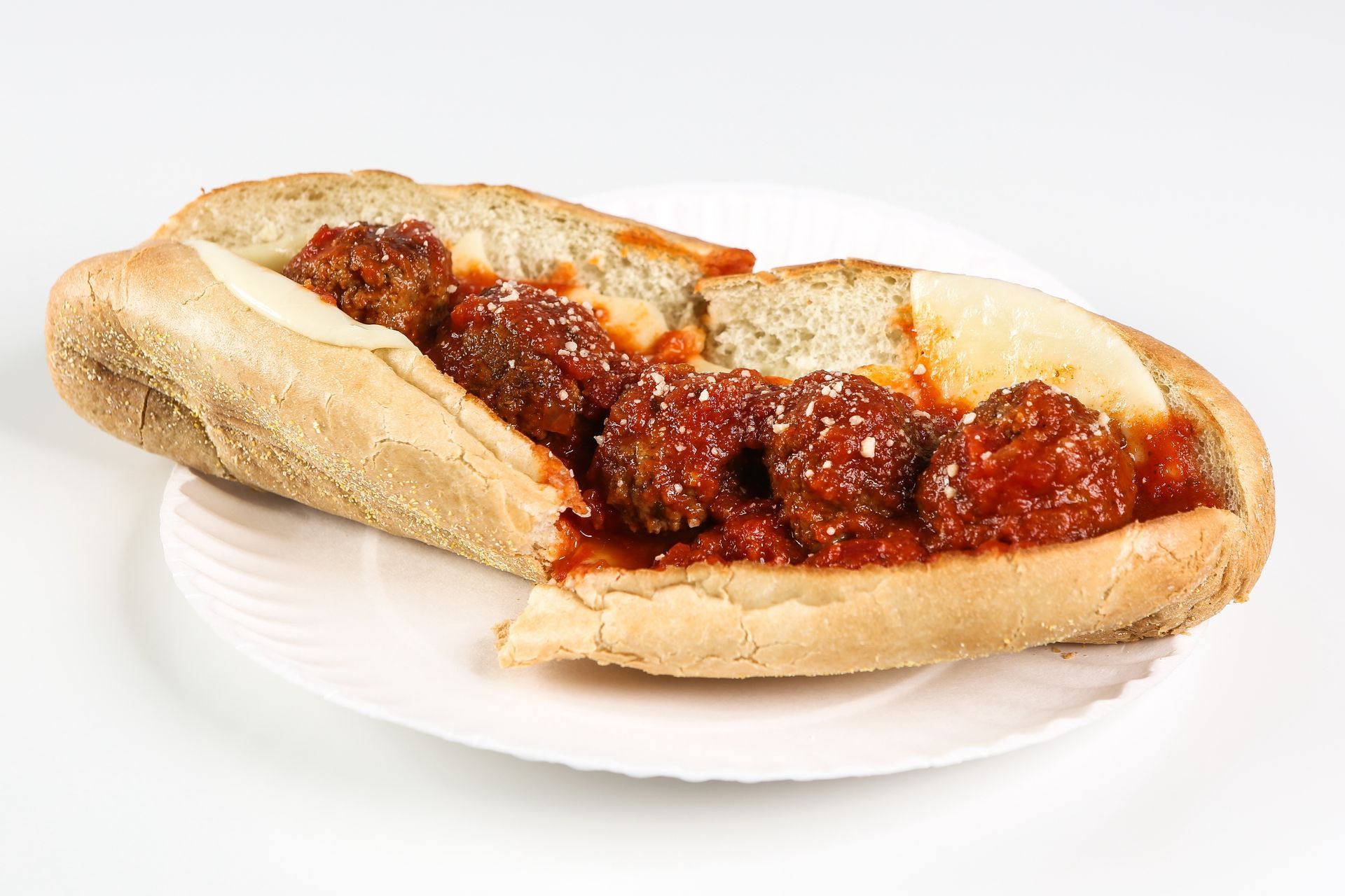 A sub sandwich with meatballs and sauce on a white plate.