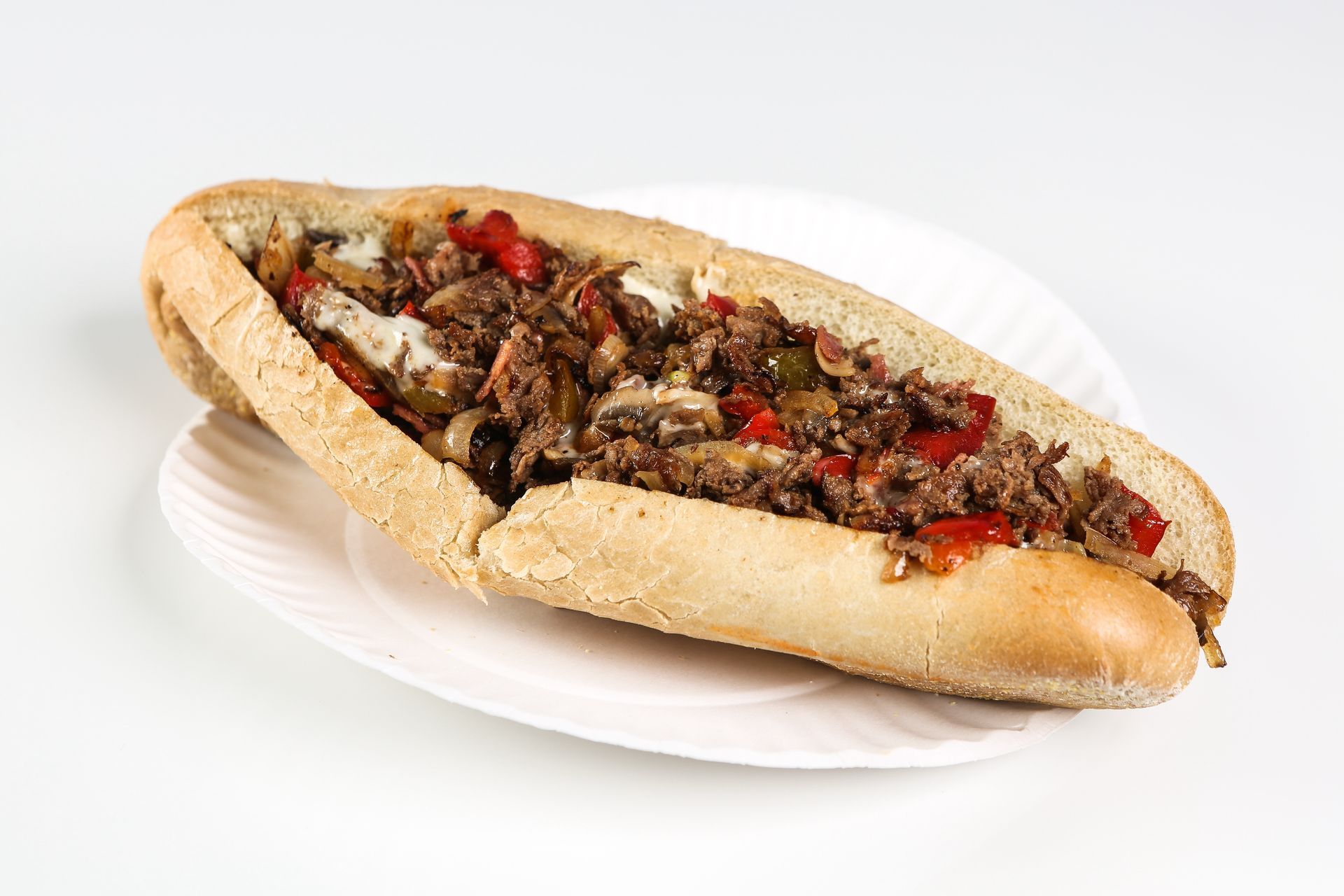 A steak sandwich on a paper plate on a white background.