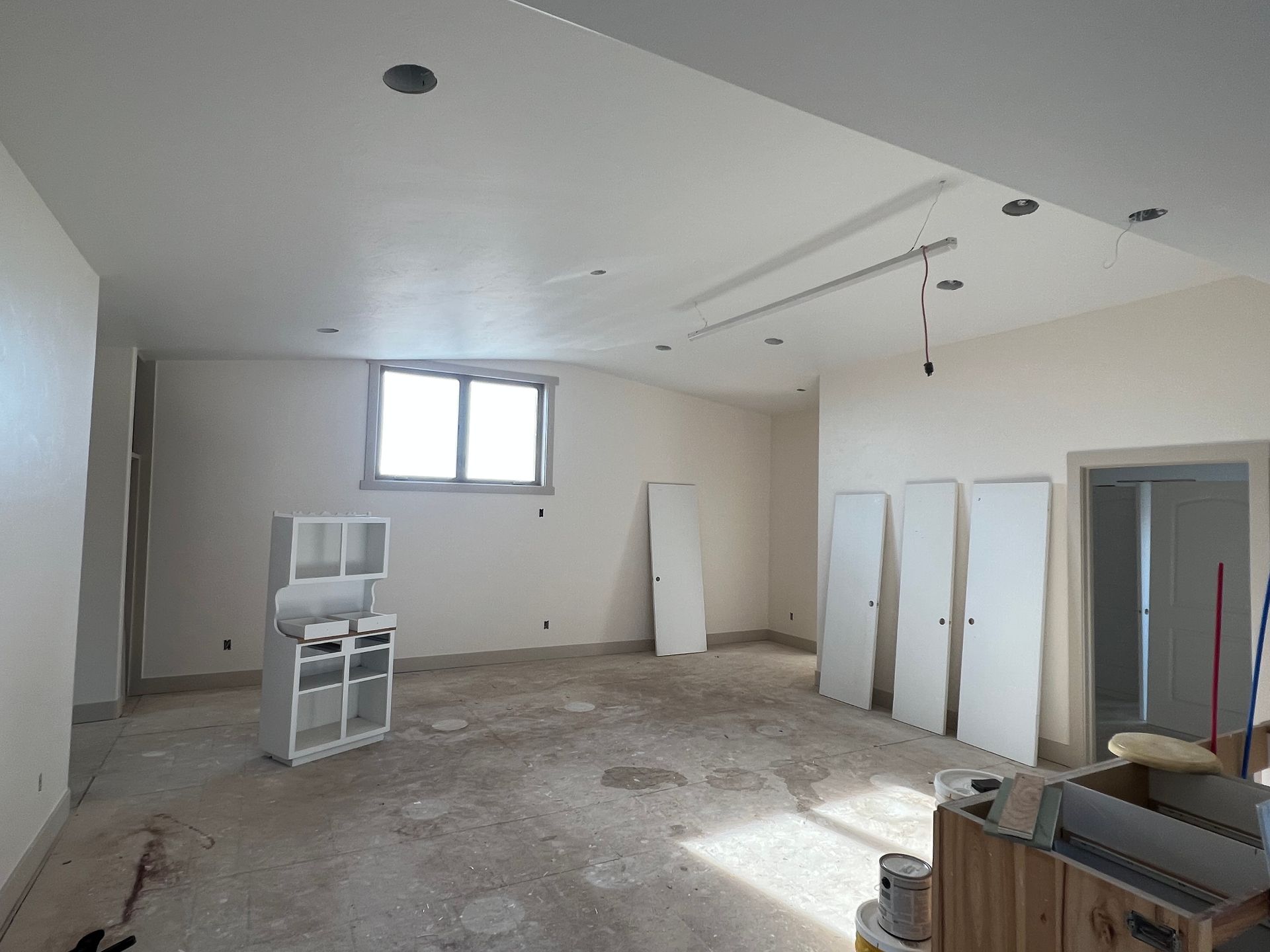 Partially renovated room with bare floors, white walls, windows, and construction materials scattered around