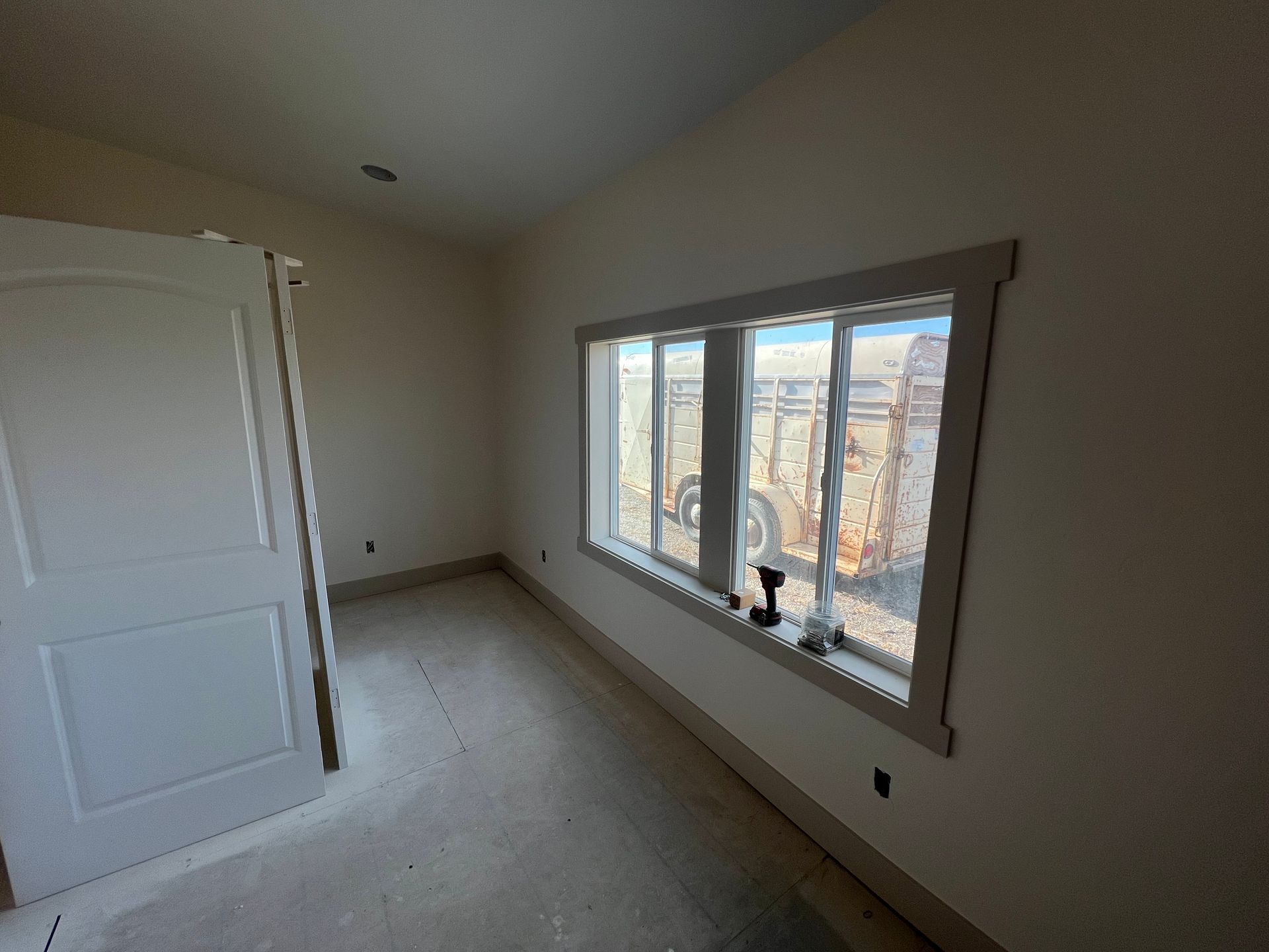 Empty beige bedroom with large window, carpeted floor, and white closet door.