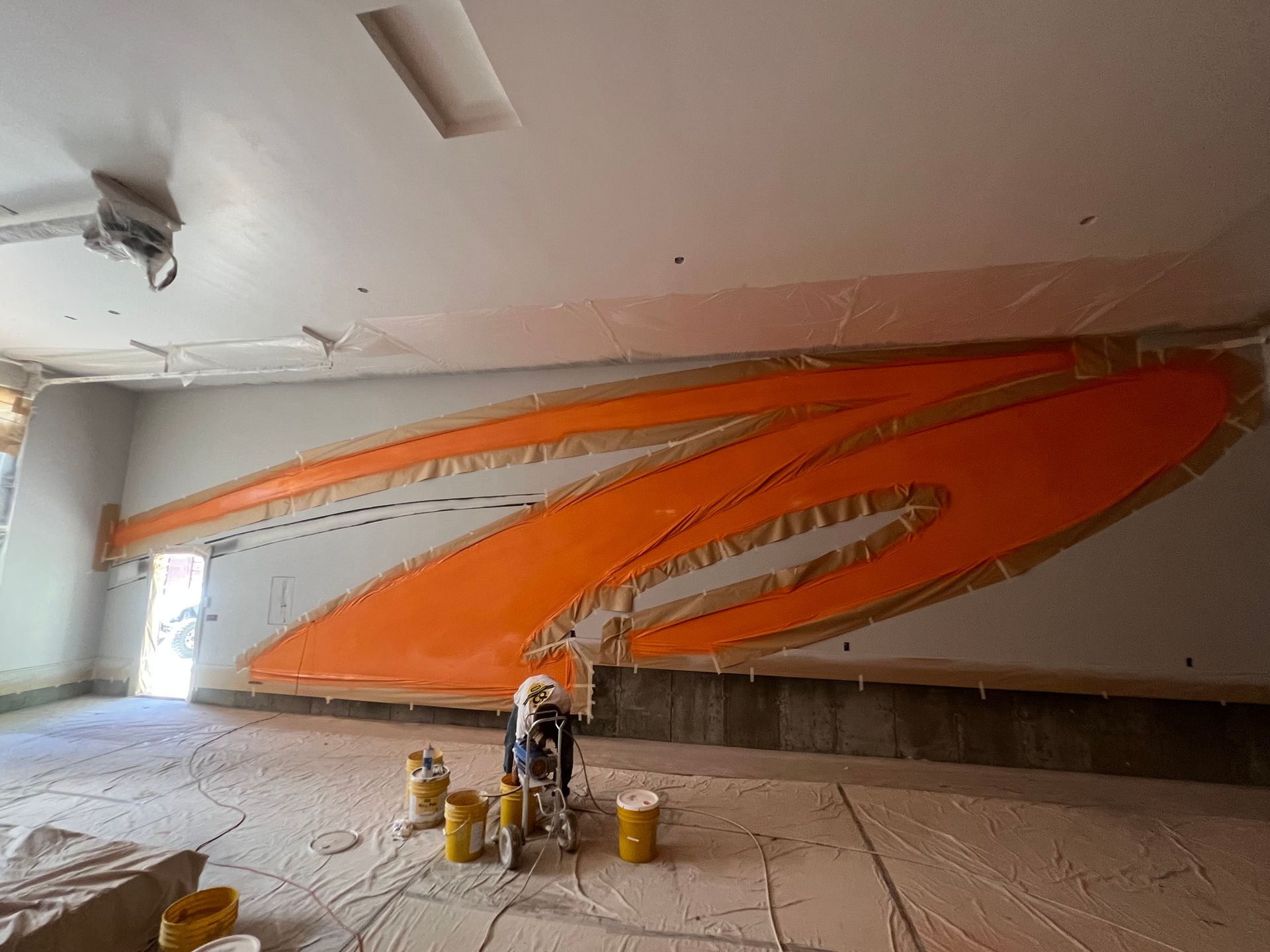 Bright orange abstract mural being painted on a large white wall in an unfinished room