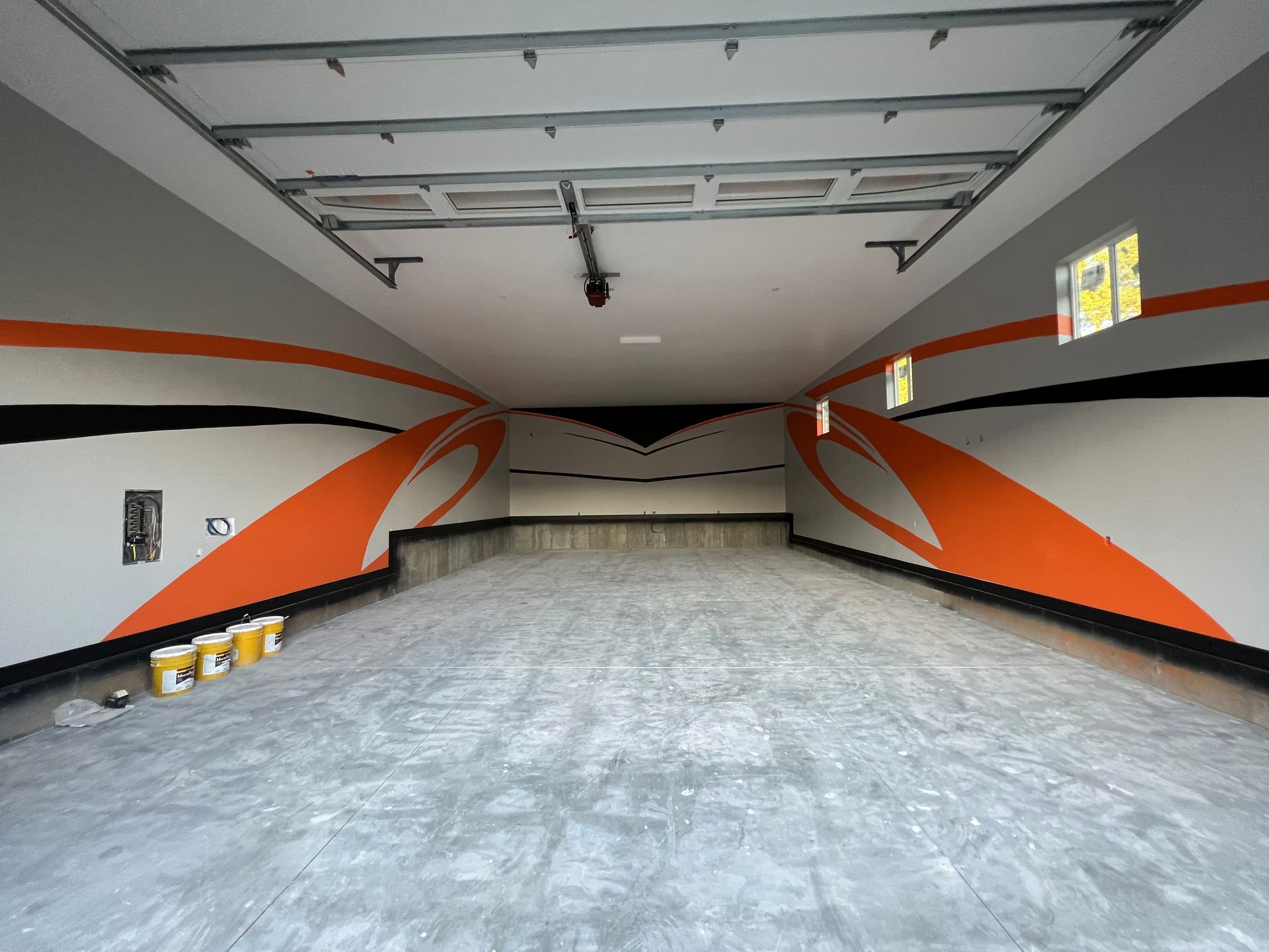 Empty garage interior with gray floor, white ceiling, and bold orange-and-black wall stripes