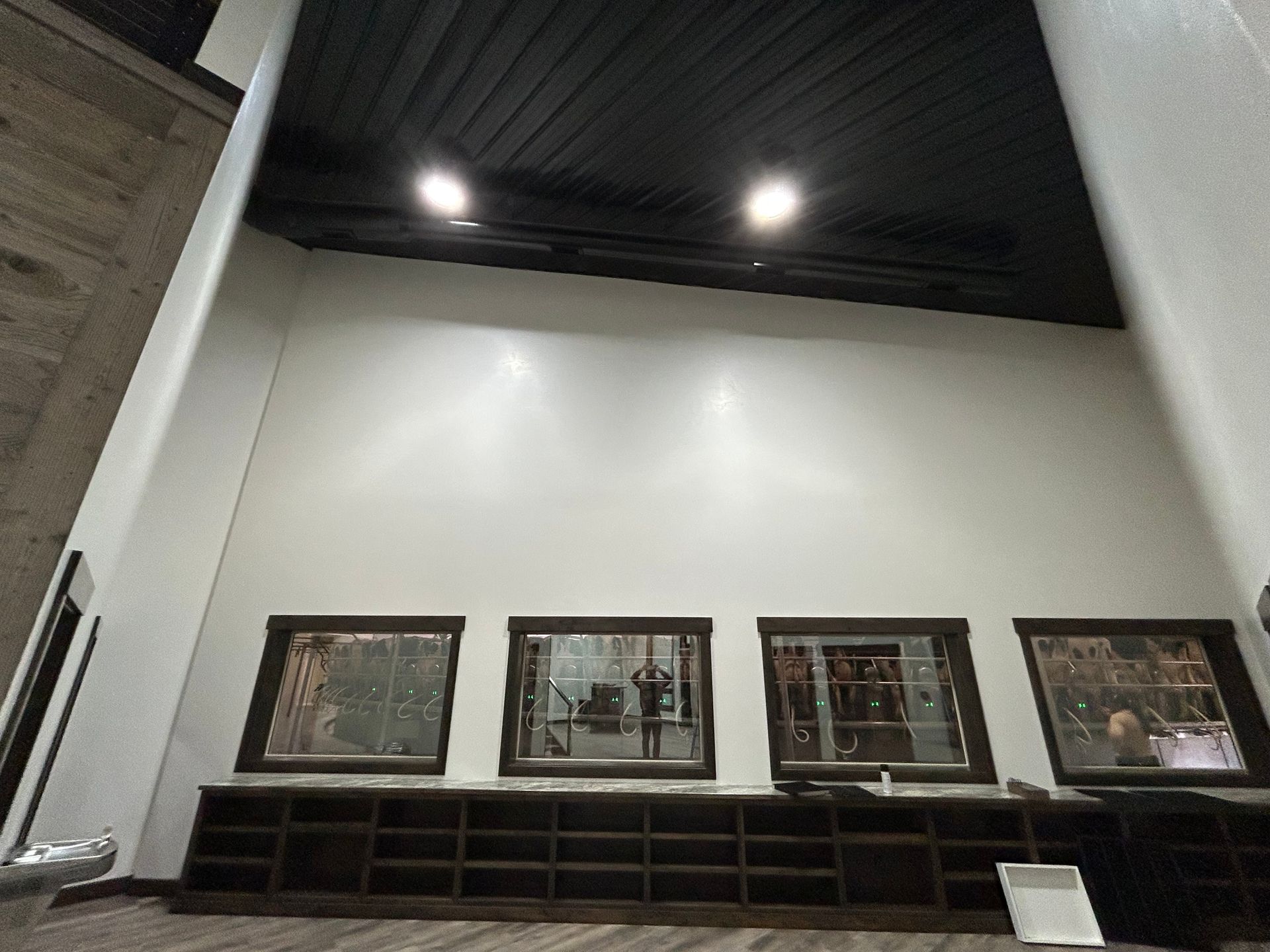 Empty modern interior with high white wall, dark ceiling lights, and low wooden shelving along the back wall