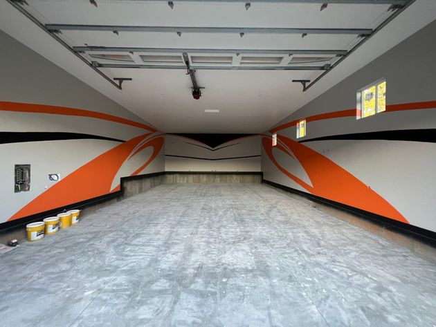 Empty garage with gray floor, white ceiling, and orange, black, and gray wall stripes