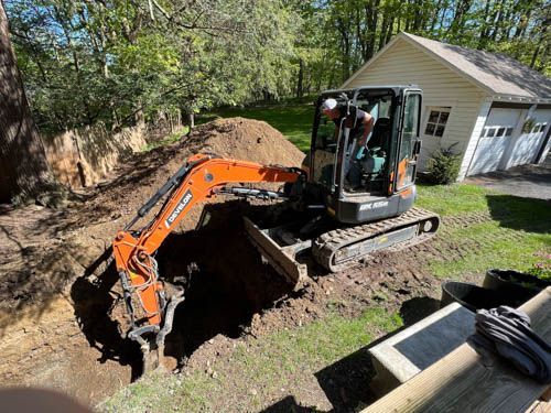 An excavator is digging a hole in the dirt in front of a house.