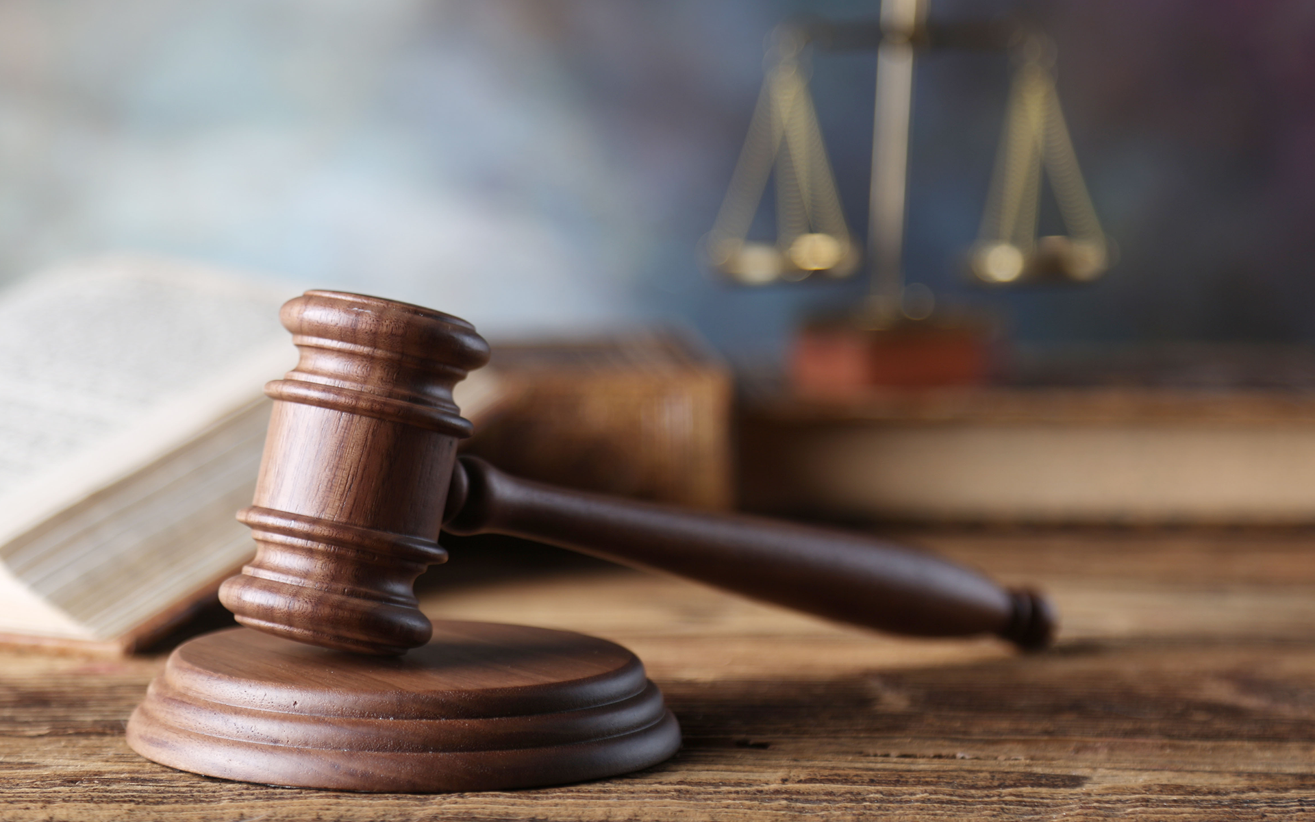 A wooden judge 's gavel is sitting on a wooden table next to a book and scales of justice.