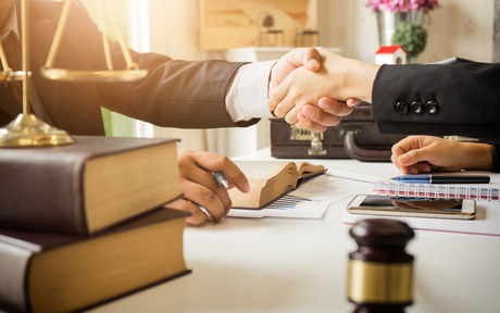A lawyer is shaking hands with a client in front of a gavel.