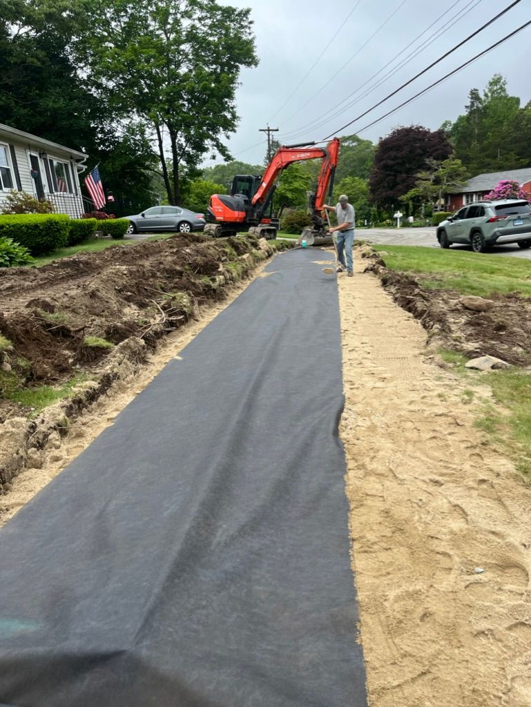 Construction site with an excavator, a long trench covered with black fabric, and a worker.