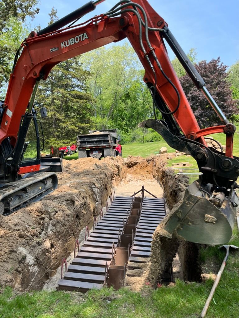 Red Kubota excavator digging a trench, revealing metal structural elements, likely for construction.