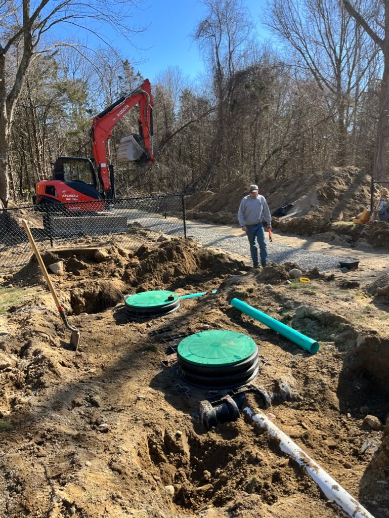Excavation site with a man, an excavator, and two septic tank lids.