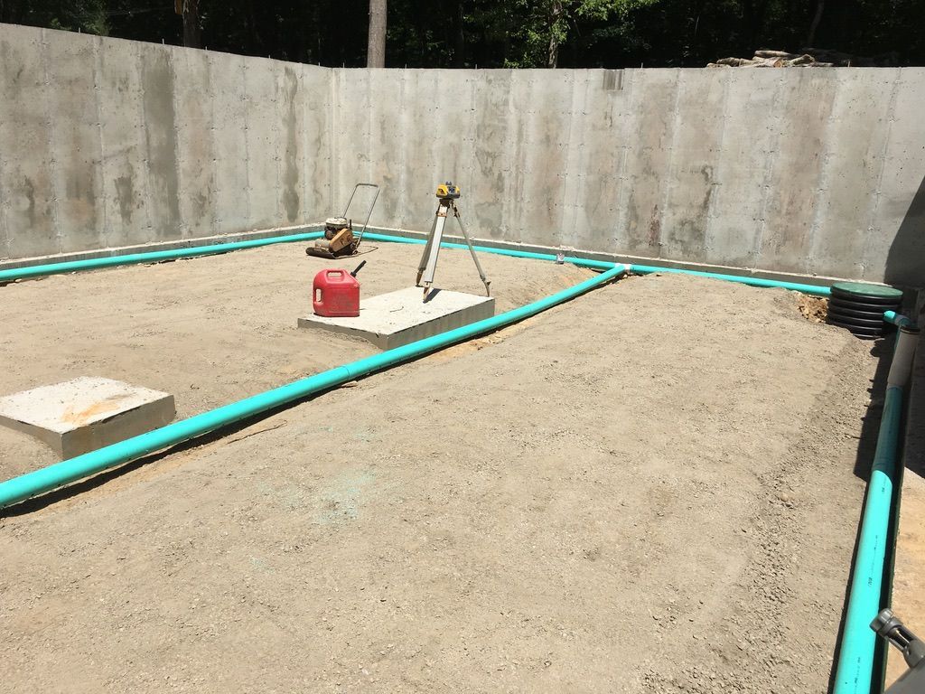 Construction site: concrete walls, gravel base, blue pipes outlining a square, surveying equipment.